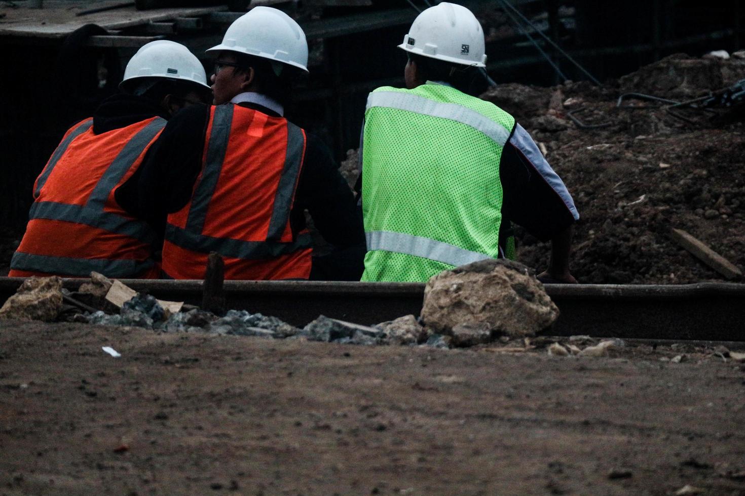 Jakarta, Indonesia in July 2022. Three construction workers are resting to unwind after work by sitting on the edge of the construction site photo