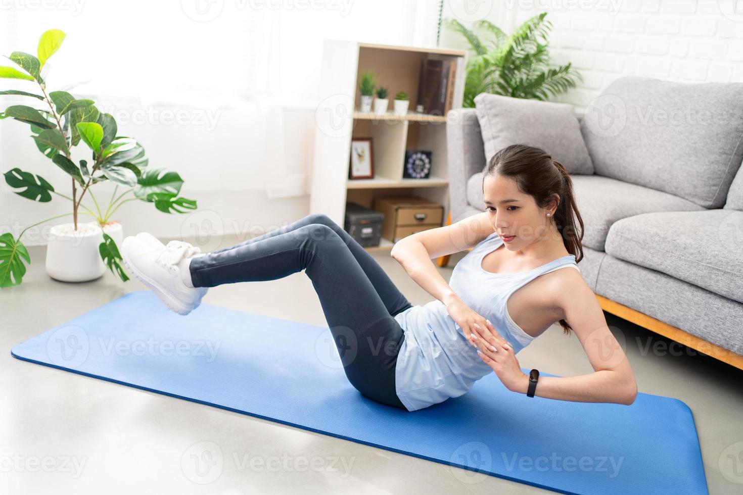 Asian young healthy woman exercising on yoga mat at home, she is doing a Russian twist. photo