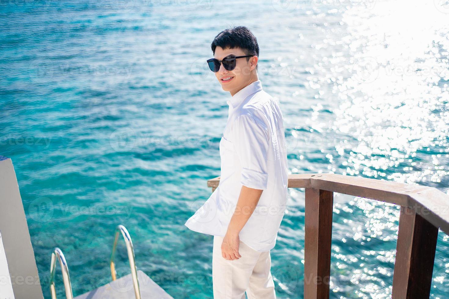 Happy asian man in sunglasses standing at sea on vacation photo