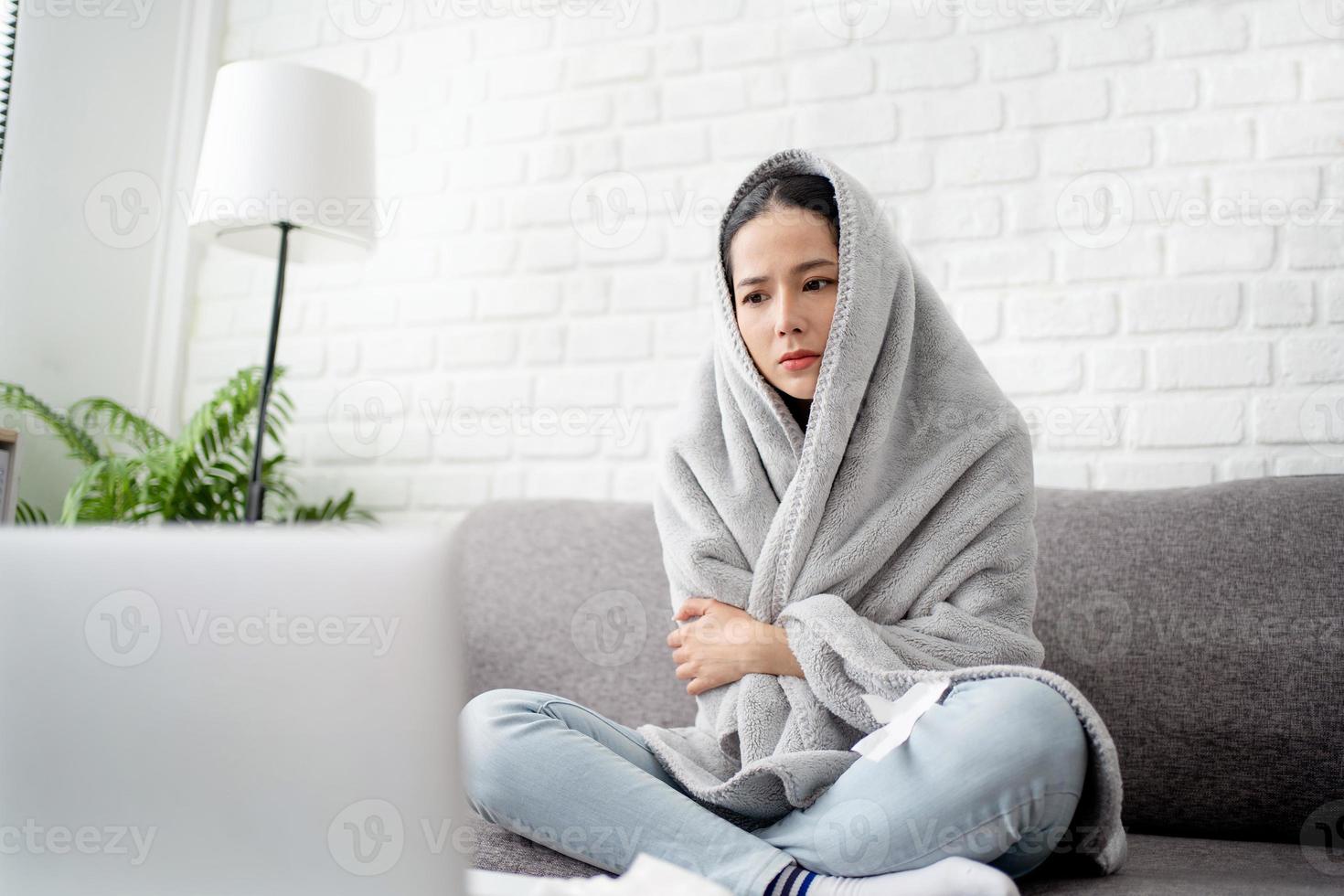 Upset young woman freezing, feeling cold at home, sitting on sofa covered with blanket photo