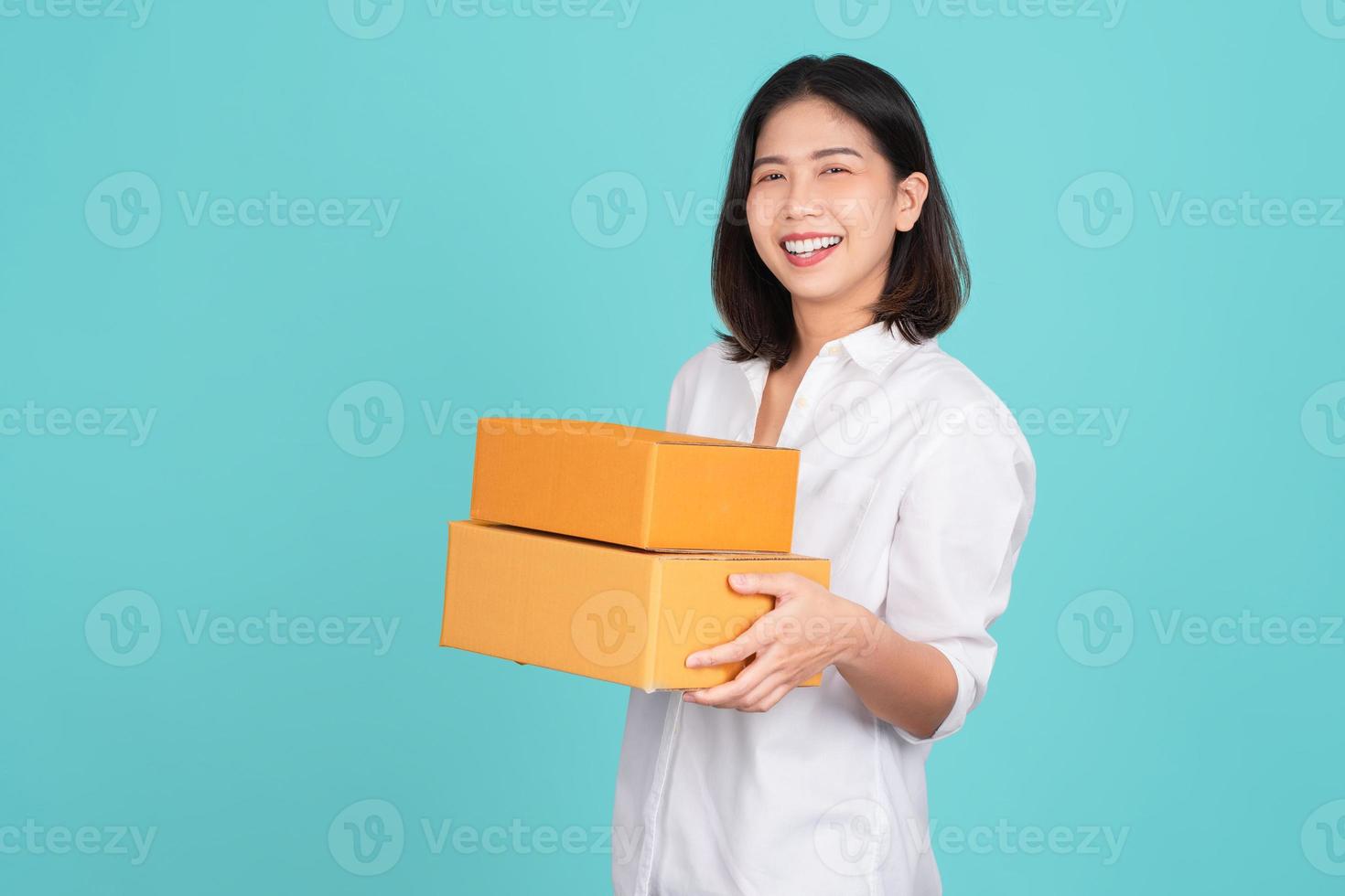 Happy Asian woman smiling wearing white shirt and holding package parcel box isolated on white background, Delivery courier and shipping service concept photo