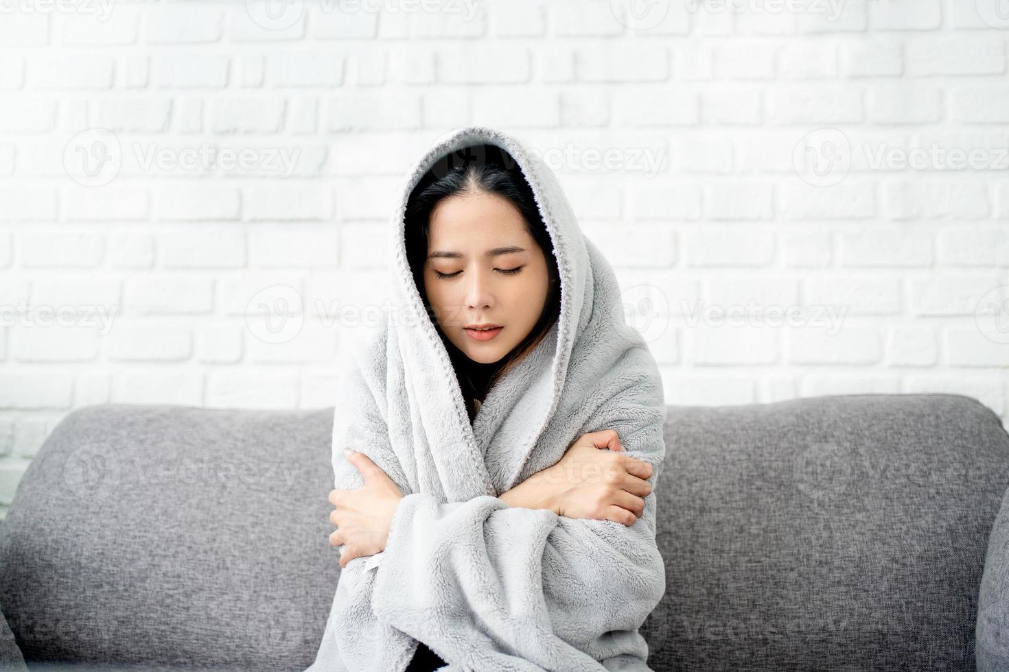 Close up sick asian woman covered with blanket sitting on couch, ill young female in warm suffering from fever, catch cold or flu, virus symptoms photo