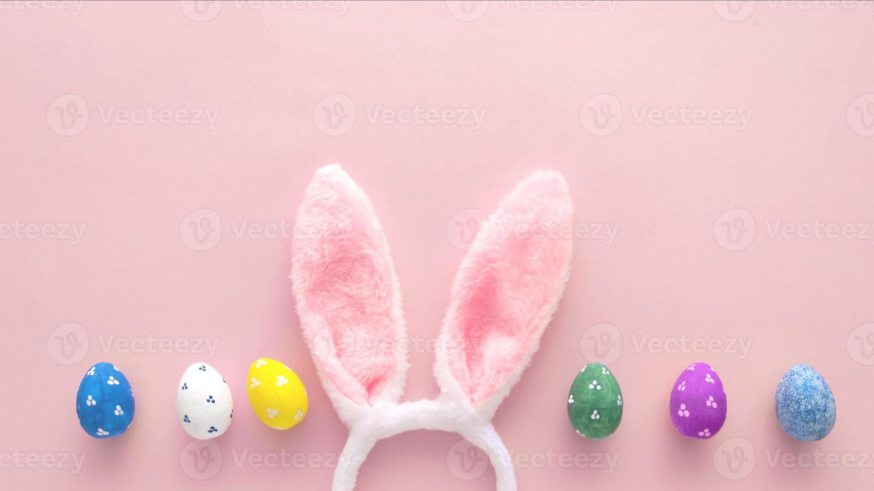 Decorated Easter eggs and bunny ears on color pink background, top view photo