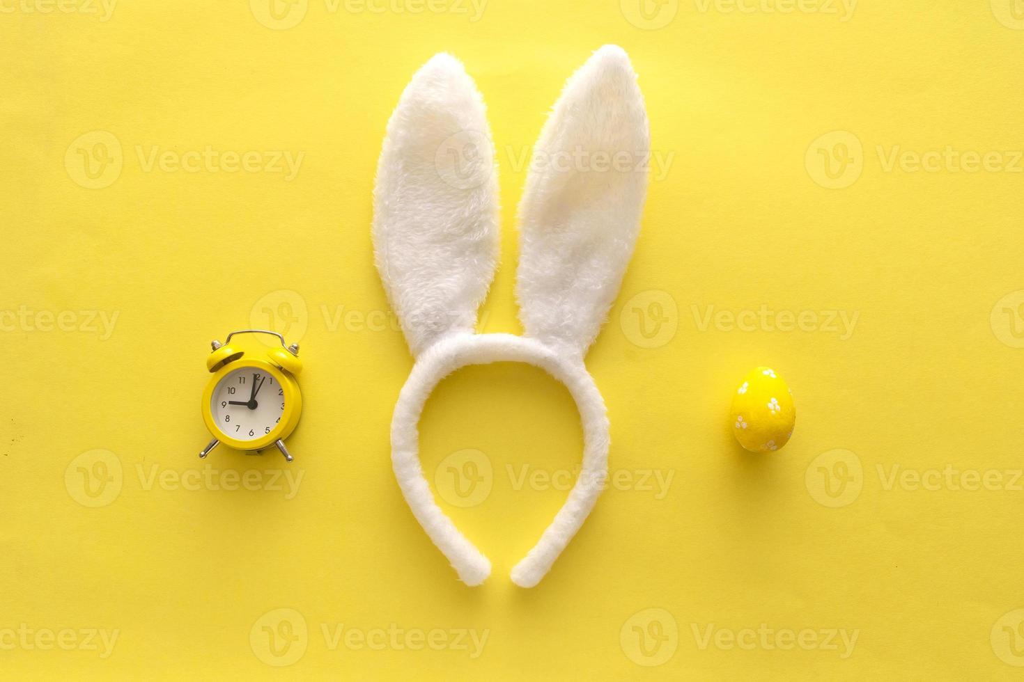Decorated Easter eggs and bunny ears on color yellow background, top view photo