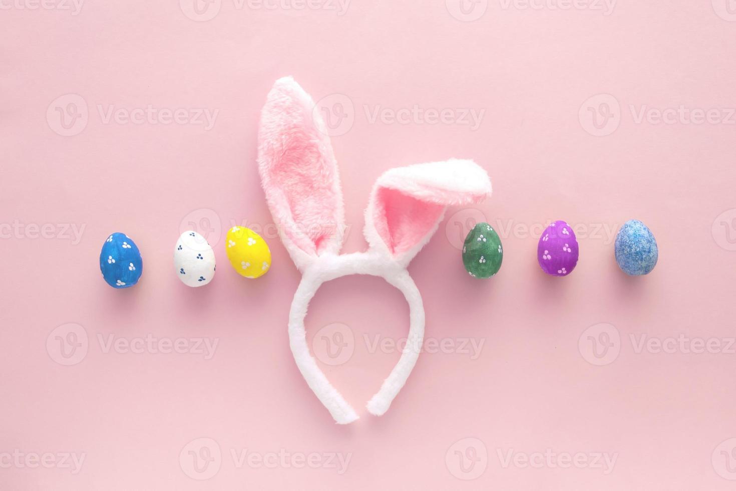 Decorated Easter eggs and bunny ears on color pink background, top view photo