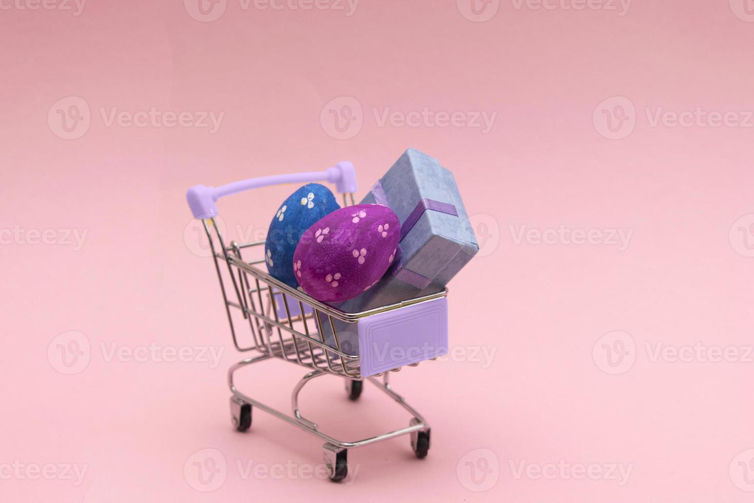 huevos de pascua coloridos en el carrito de compras sobre fondo rosa. copie el espacio para el texto. foto