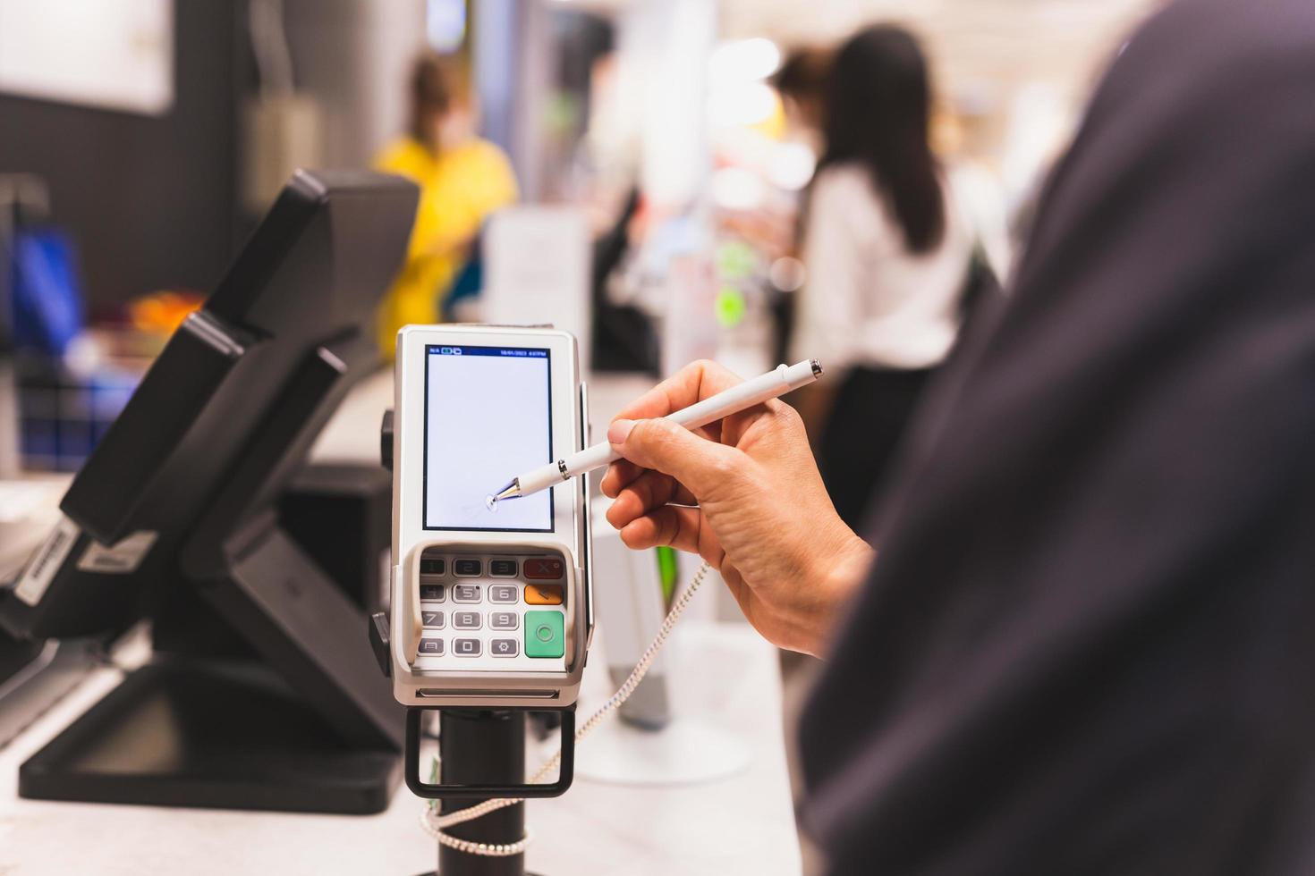 las mujeres de los consumidores firman en una pantalla táctil de la máquina de transacciones con tarjeta de crédito en el mercado de la cena. foto