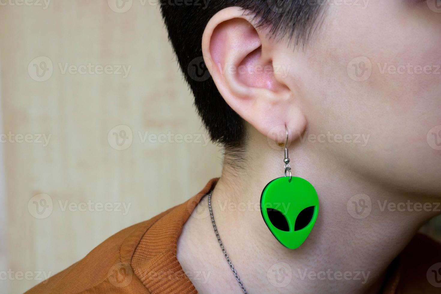 Earring in the form of a green alien head in the girl's ear close-up photo