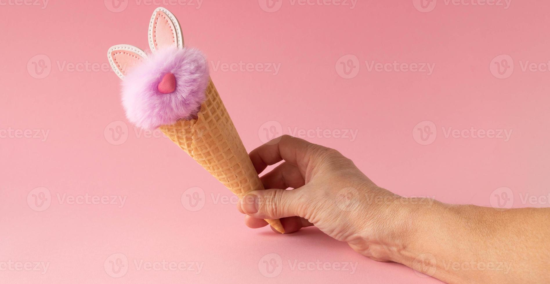 Abstract pink background. A hand with a fluffy lilac rabbit in a waffle cone. The concept of love, a greeting card for Valentine's Day and Easter photo