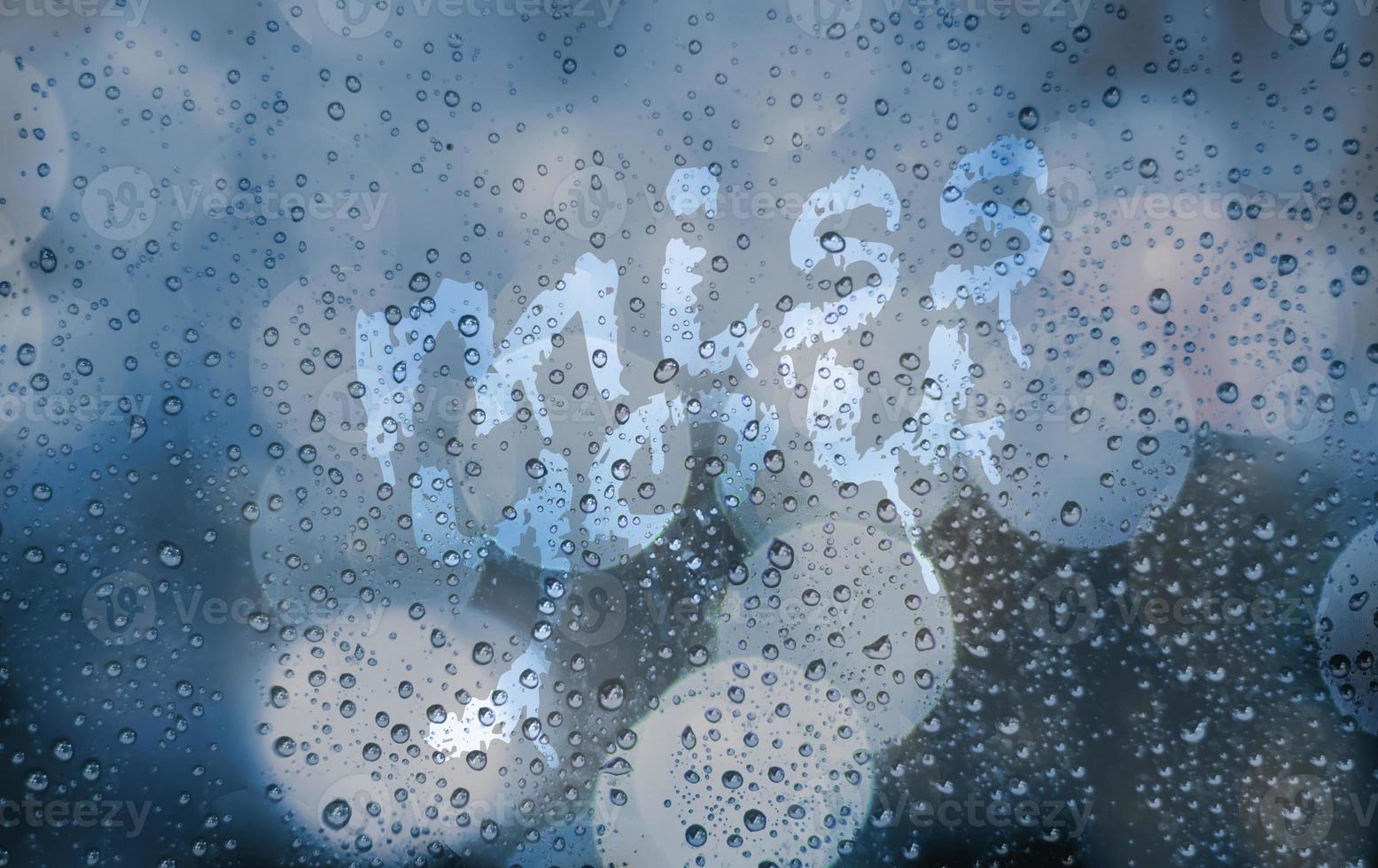 Miss you on wet window glass. Blue blurred grainy background with city light and bokeh. Glass with raindrops and stains from finger drawing. Abstract aesthetic backdrop. Romantic emotion , lonely photo