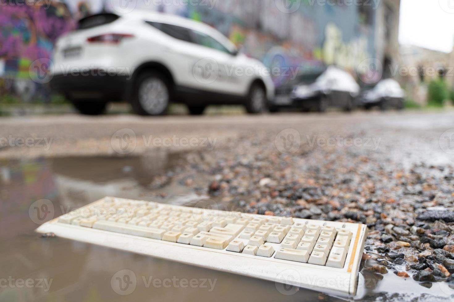 old broken computer keyboard, thrown into the trash lying on the road in a puddle. photo