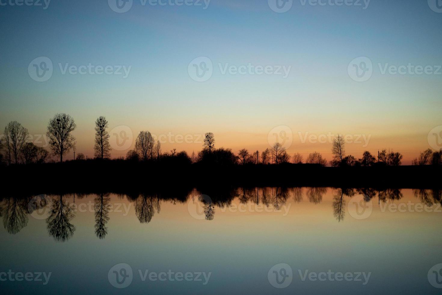 silhouette and reflection of trees by the lake at sunset photo