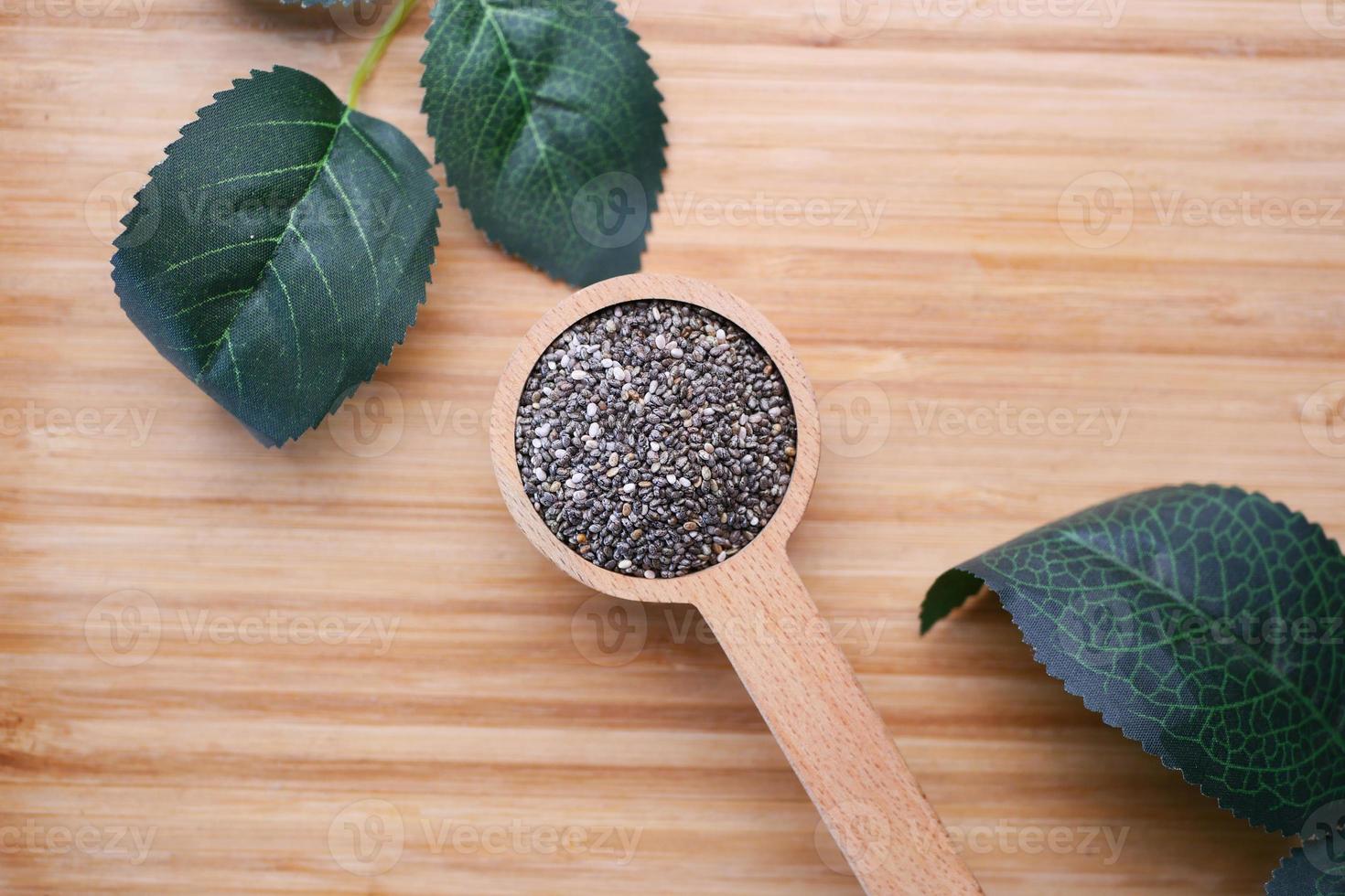 top view of chia seed in a wooden spoon and leaf on table photo