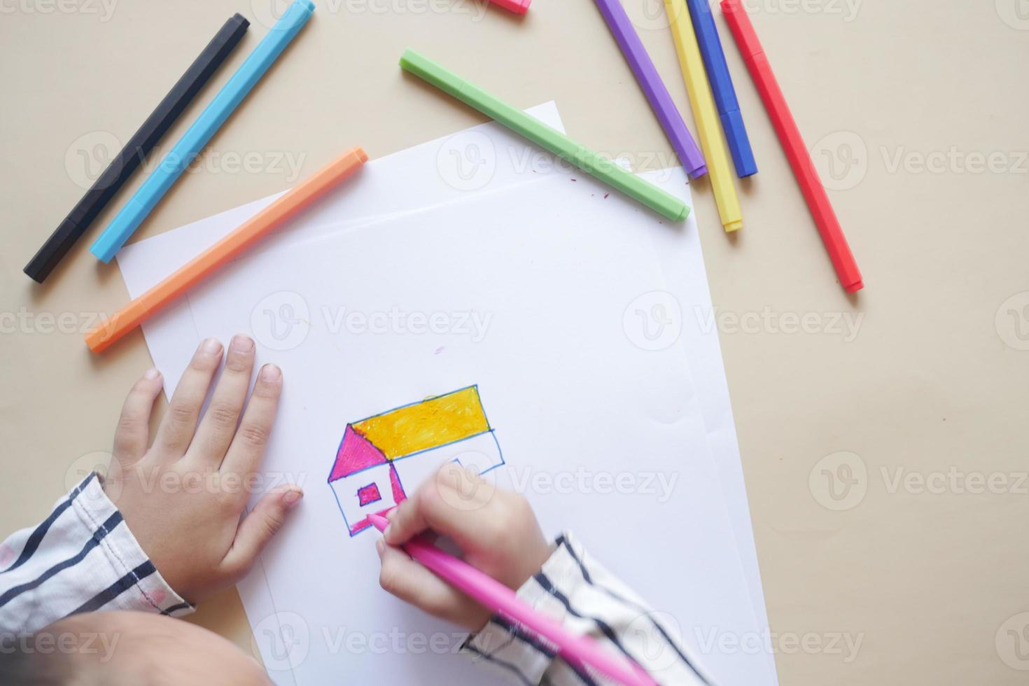 top view of child girl drawing a house with color pencils on paper photo