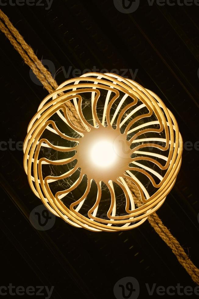 Bottom view of yellow bulb with rattan woven ornament that hanging in the rope. Inspiration for modern lighting and home decoration. Rattan chandelier for vintage and abstract background. Wicker Lamp. photo