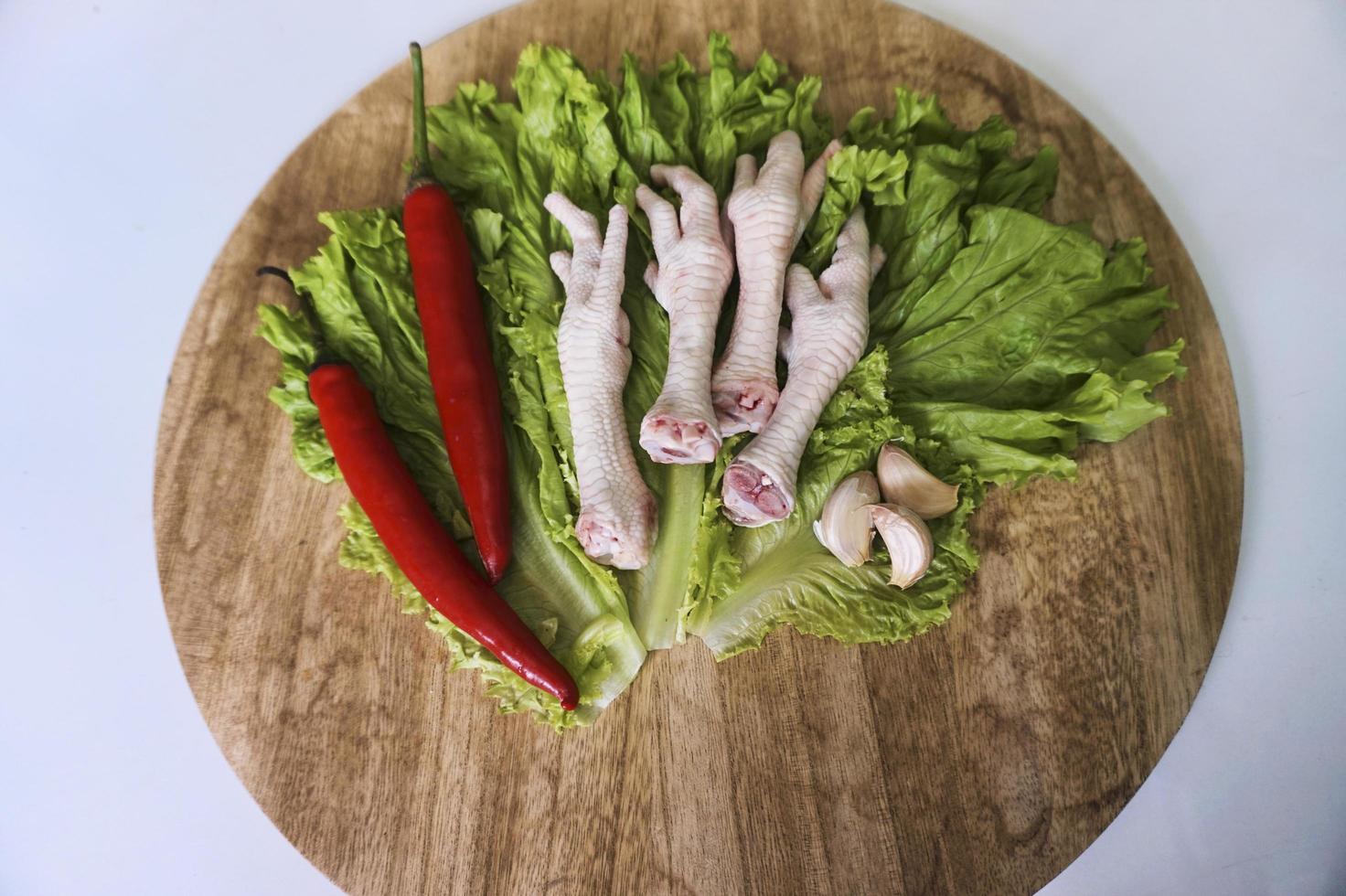 Raw chicken feets on a chopping Board with lettuce, red chilies, and garlics. Fresh and organic chicken feets. Top view photo