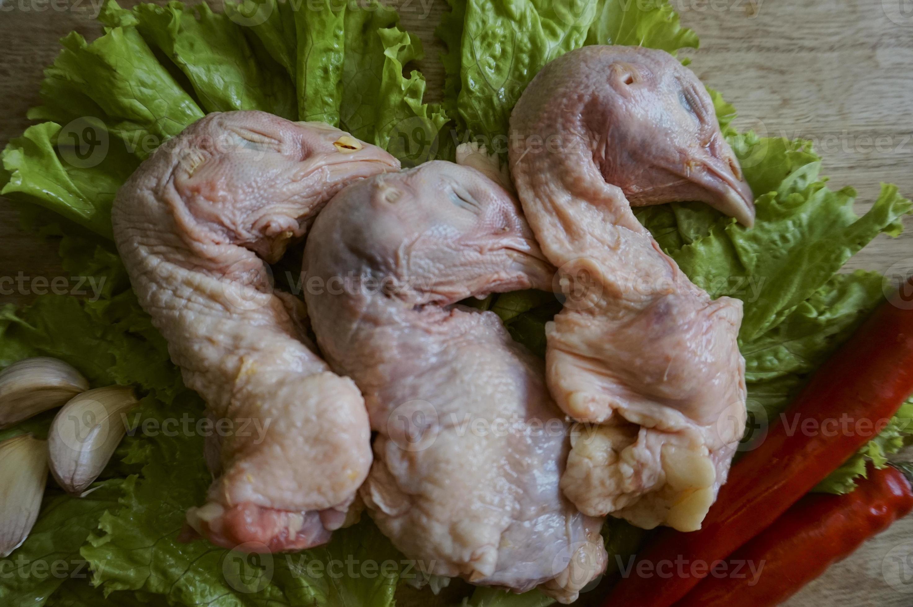 Raw chicken head on a chopping Board with lettuce, red chilies, and