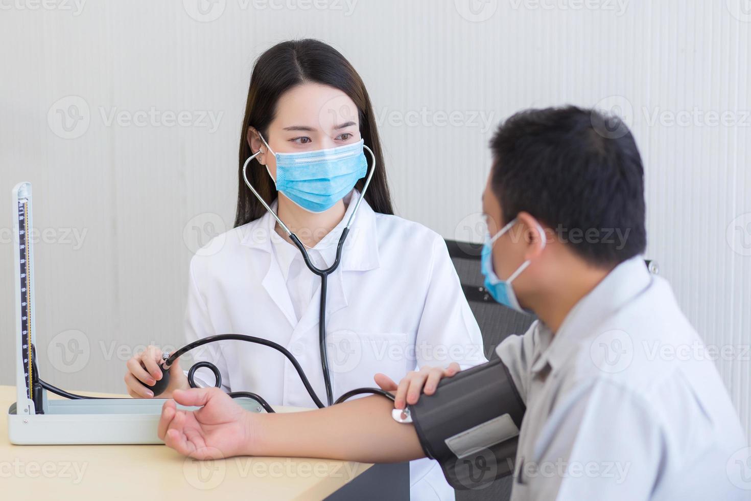 Asian woman doctor listen pulse heart rate stethoscope put on foldable joint of man patient and pump rubber of blood pressure. photo