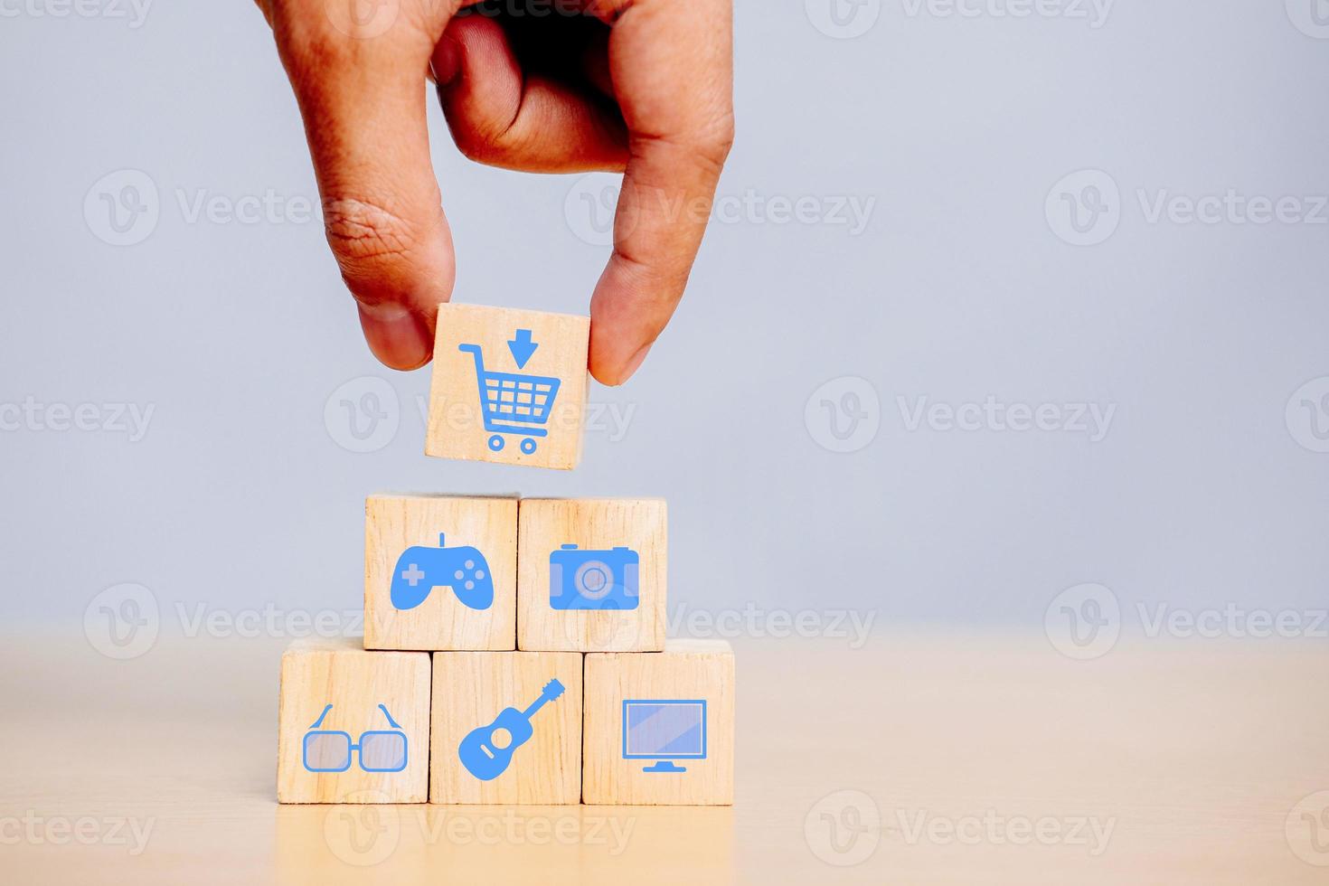 Hand holding wooden cube with cart icon joystick, camera, glasses, guitar, computer.  The concept of shopping, buying items and goods. photo