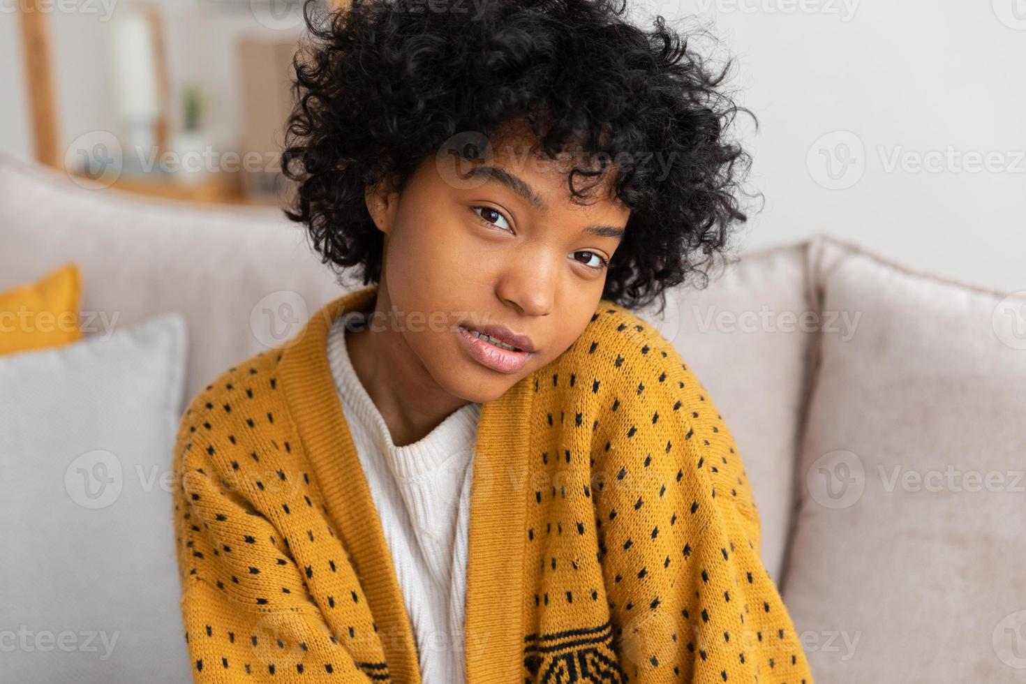 Beautiful african american girl with afro hairstyle smiling sitting on sofa at home indoor. Young african woman with curly hair laughing. Freedom happiness carefree happy people concept. photo