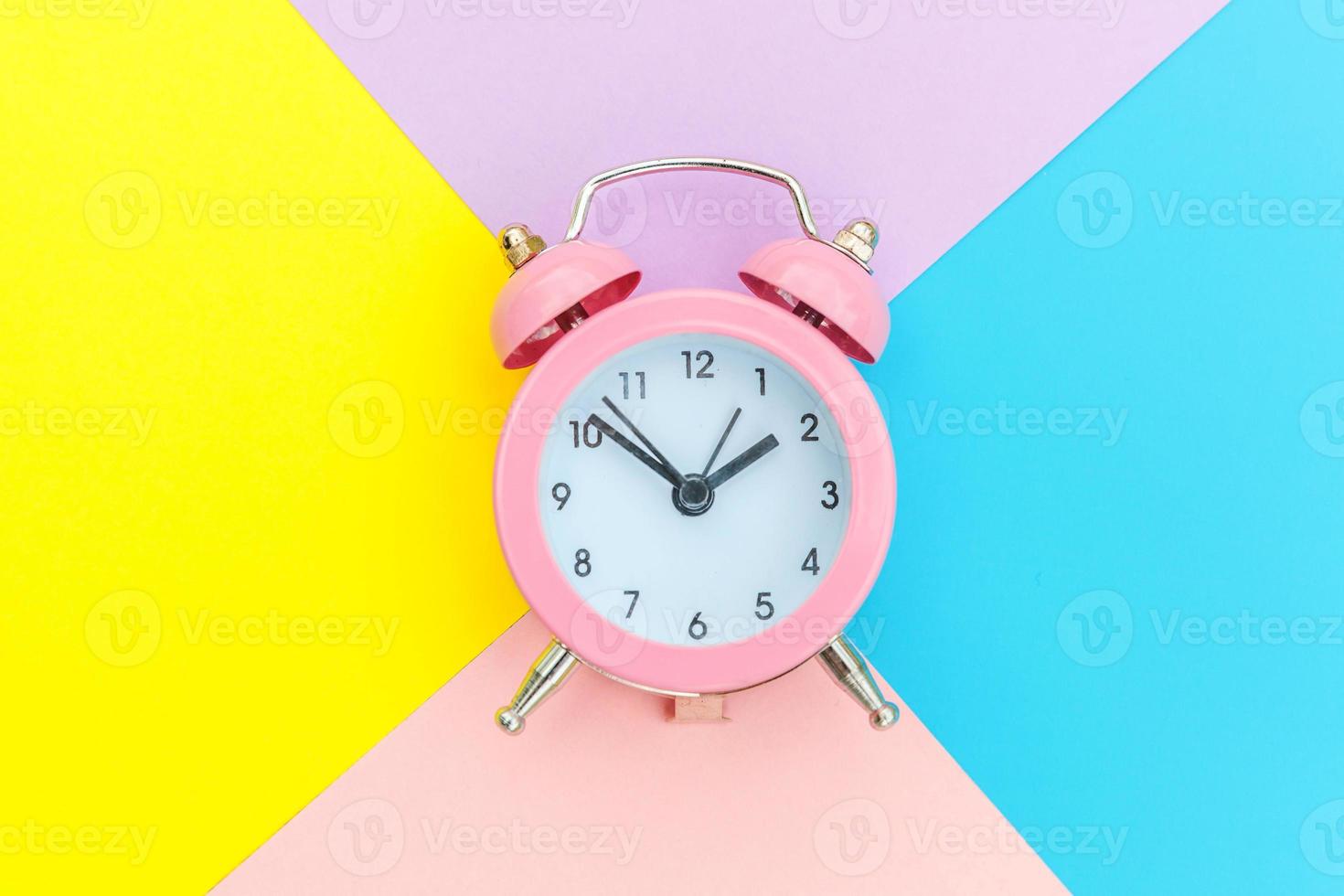 reloj despertador clásico con campana gemela aislado sobre fondo geométrico colorido azul amarillo rosa pastel. horas de descanso tiempo de vida buenos días noche despertar despierto concepto. espacio de copia de vista superior plana. foto