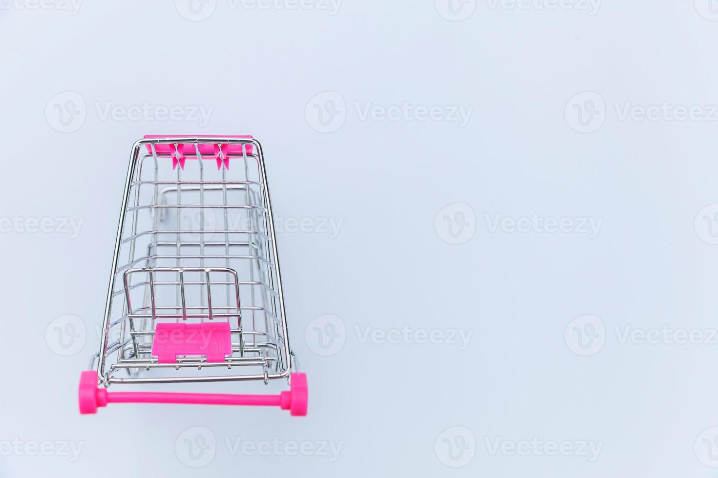 Small supermarket grocery push cart for shopping toy with wheels isolated on white background. Sale buy mall market shop consumer concept. Copy space. photo