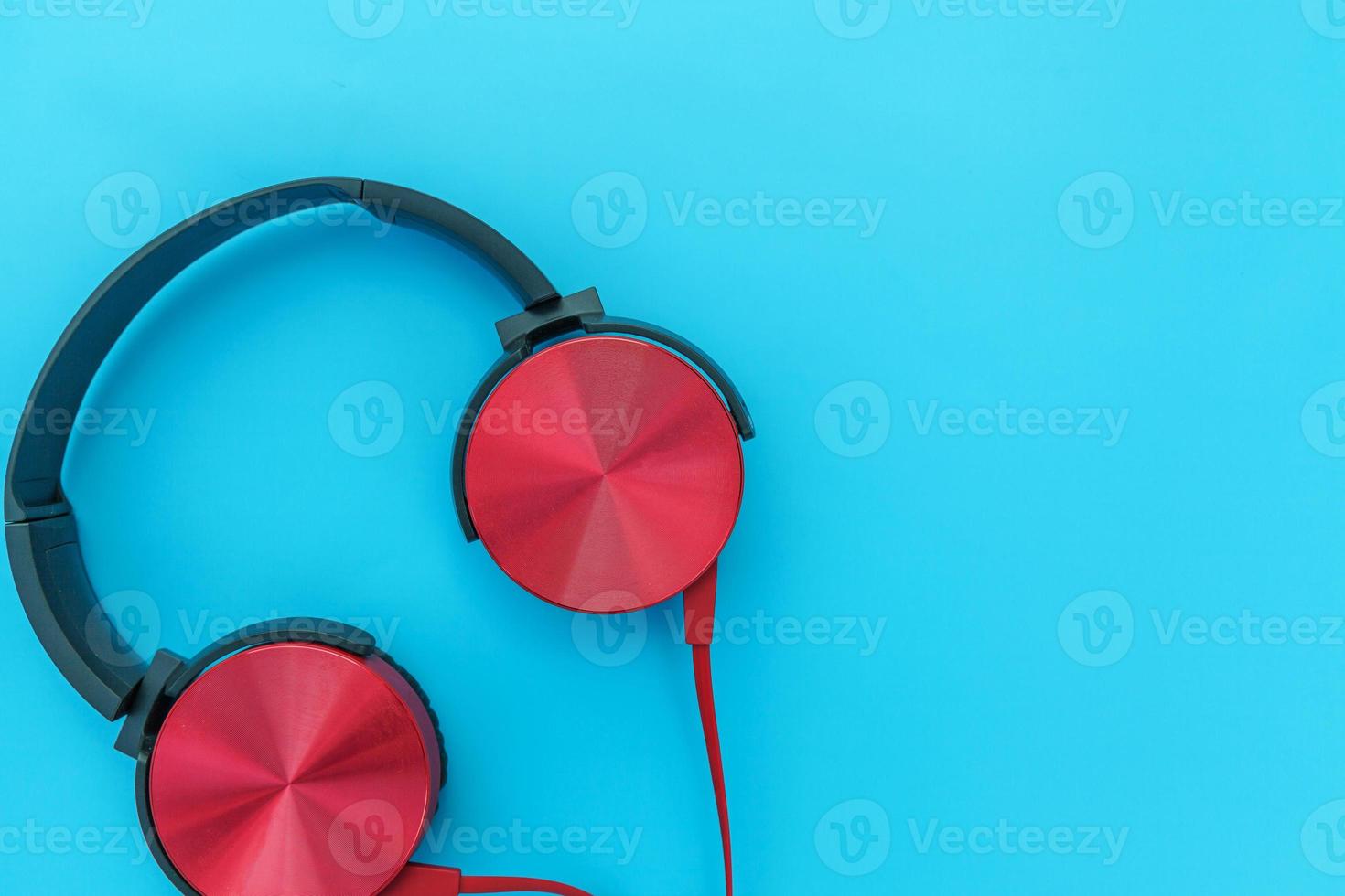 Red headphones on turquoise blue background. Minimalist simple photo of earphones with copy space. Red dj headphones with cable isolated on pastel colorful backdrop, flat lay top view. Music concept.