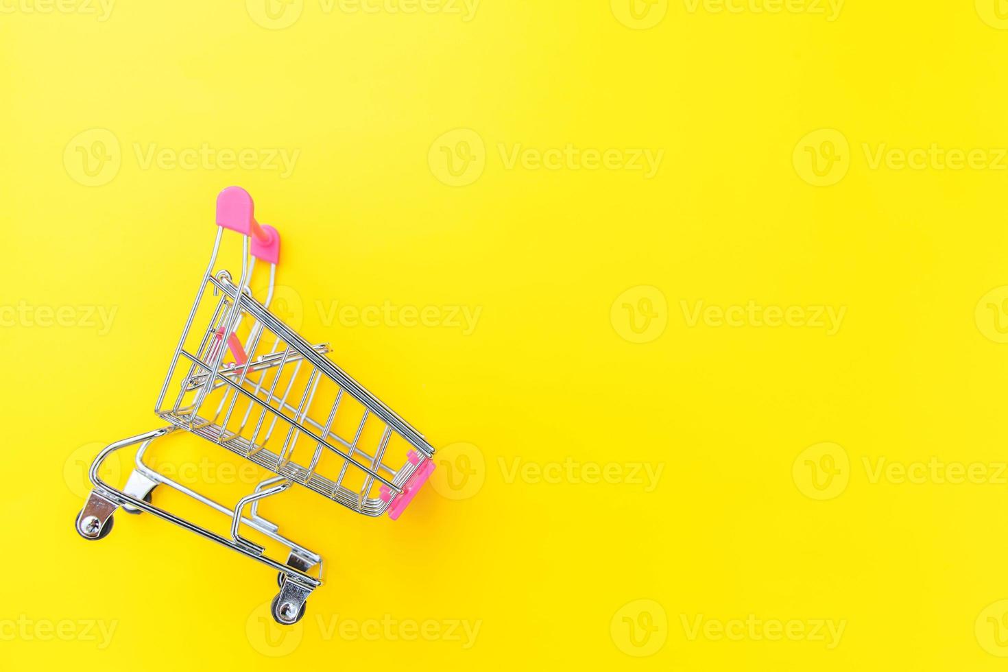 Small supermarket grocery push cart for shopping toy with wheels isolated on yellow colourful trendy modern fashion background. Sale buy mall market shop consumer concept. Copy space. photo