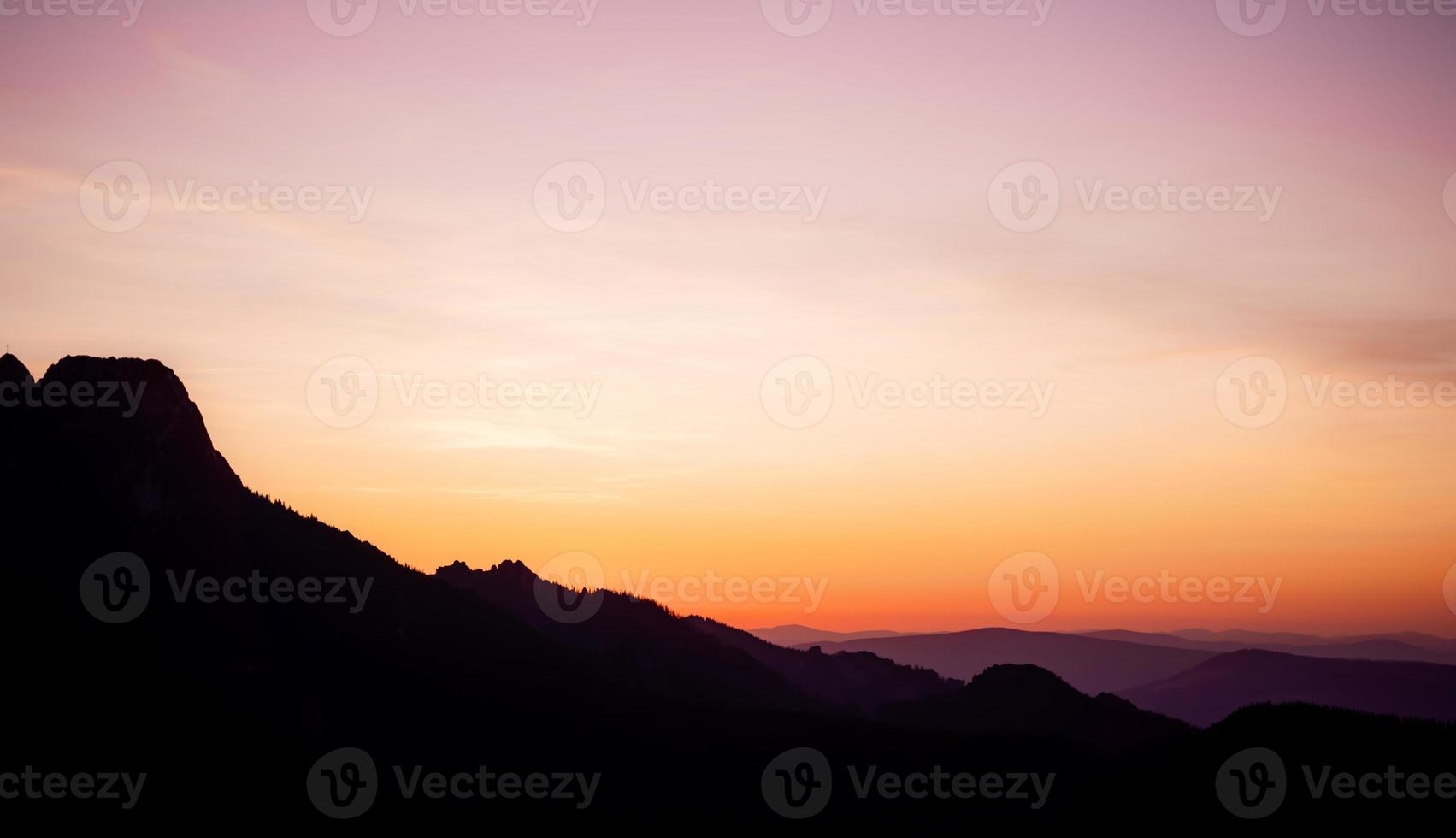 Romantic purple and orange sunset over the high Tatra mountains with dense mist and long sun rays. Vibrant and colorfull sunrise from the peak. Trekking during golden hour in the forest. photo