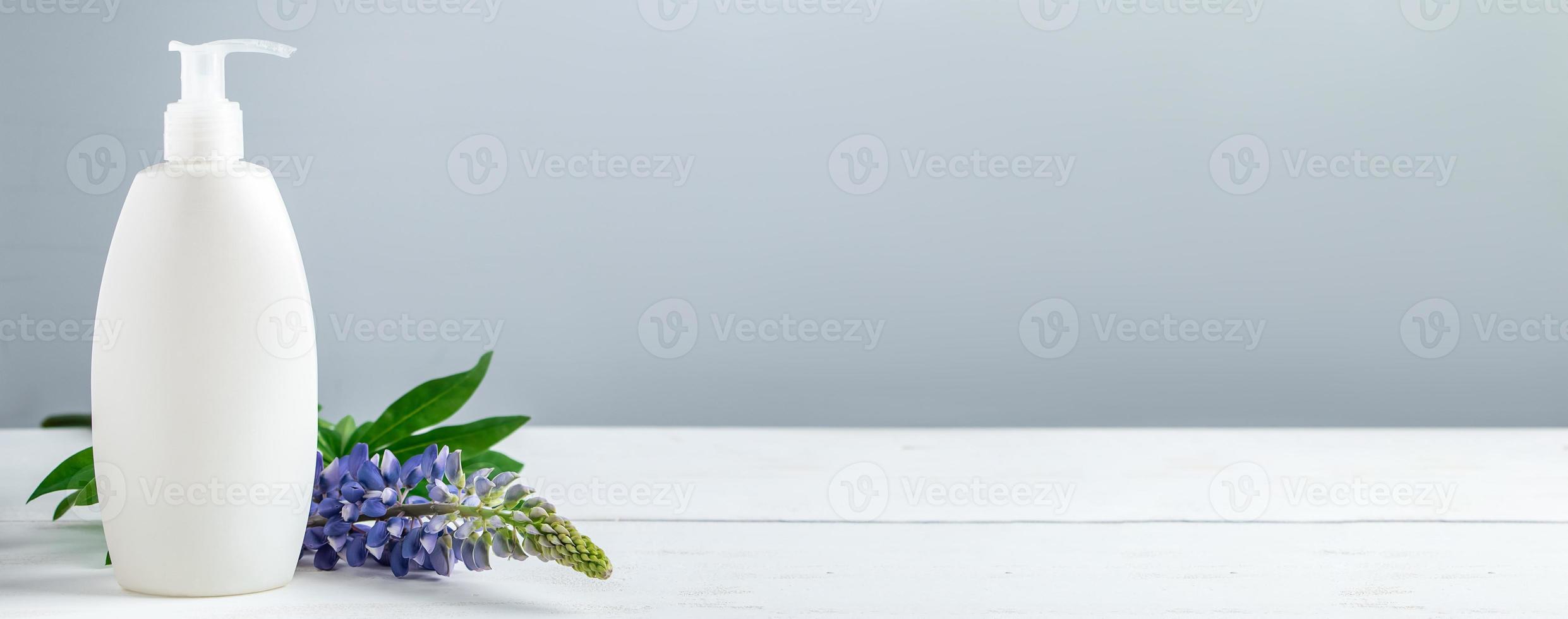 Cosmetic bottle with lotion and lupine flowers on gray background. photo
