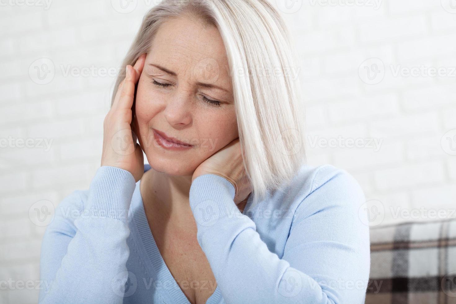 mujer que sufre de estrés o dolor de cabeza haciendo una mueca de dolor mientras sostiene la parte posterior de su cuello con la otra mano en la sien, con copyspace. foto conceptual que indica la ubicación del dolor.