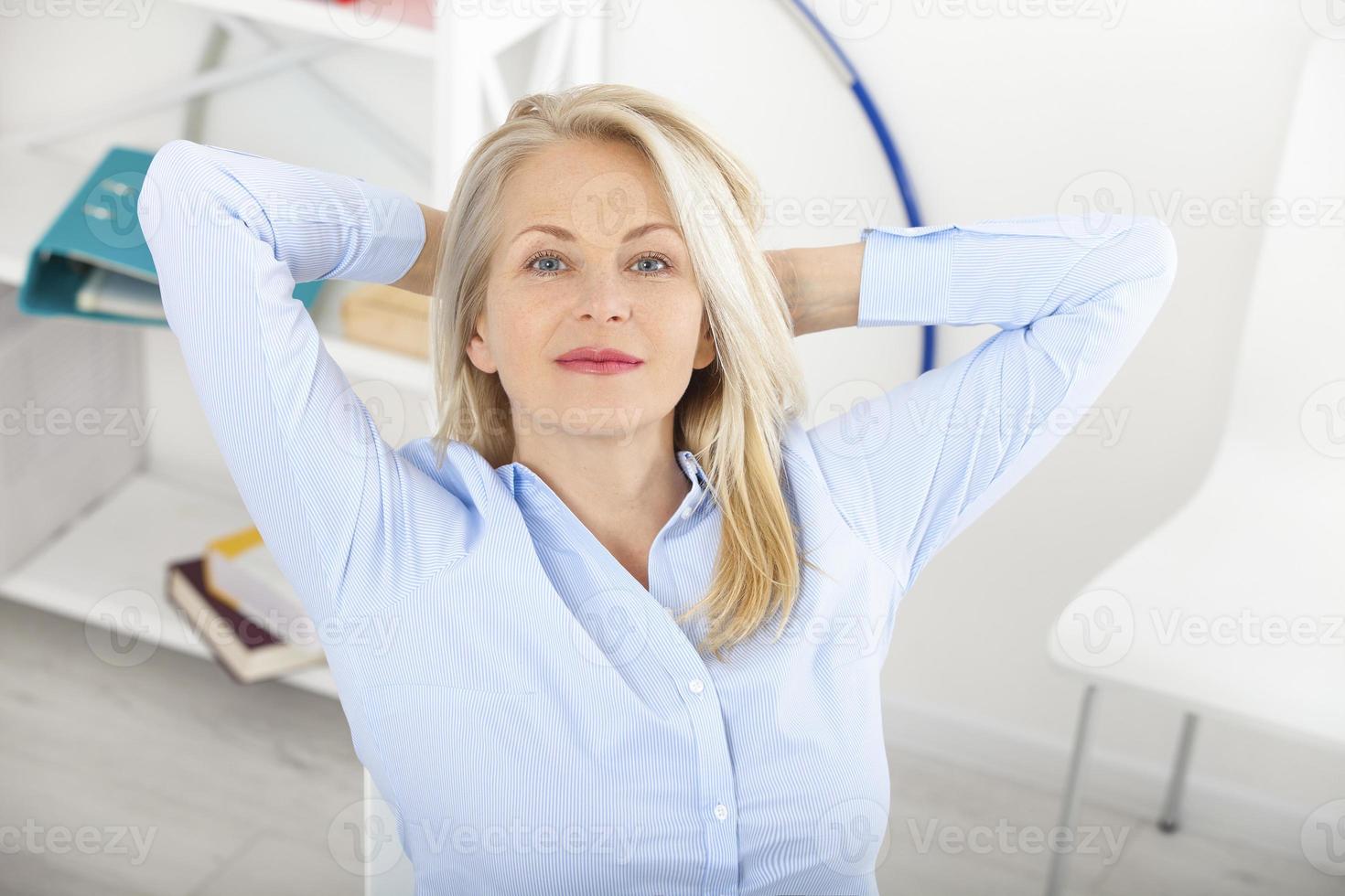 Modern businesswoman relaxed in dreams. Beautiful middle aged woman looking at camera with smile while siting in the office. photo