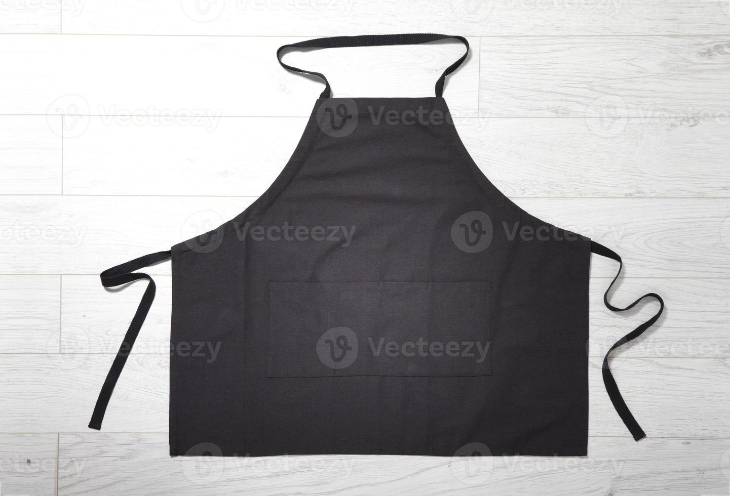 Black apron for kitchen top view on white wooden background. photo