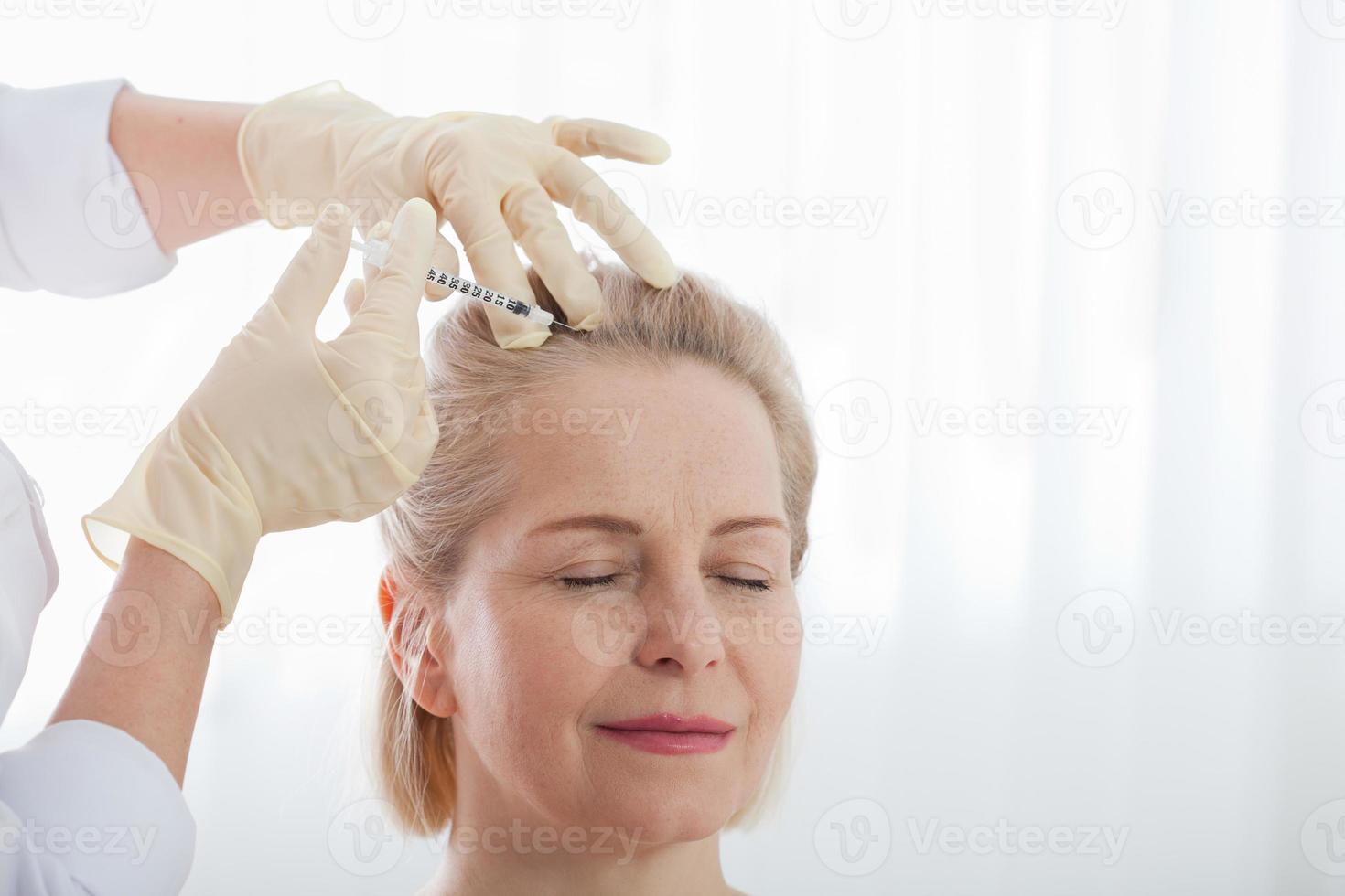 Middle aged woman gets cosmetic injection in her forehead. Hyaluronic acid injection for facial rejuvenation procedure. Woman in beauty salon. Plastic surgery clinic. photo