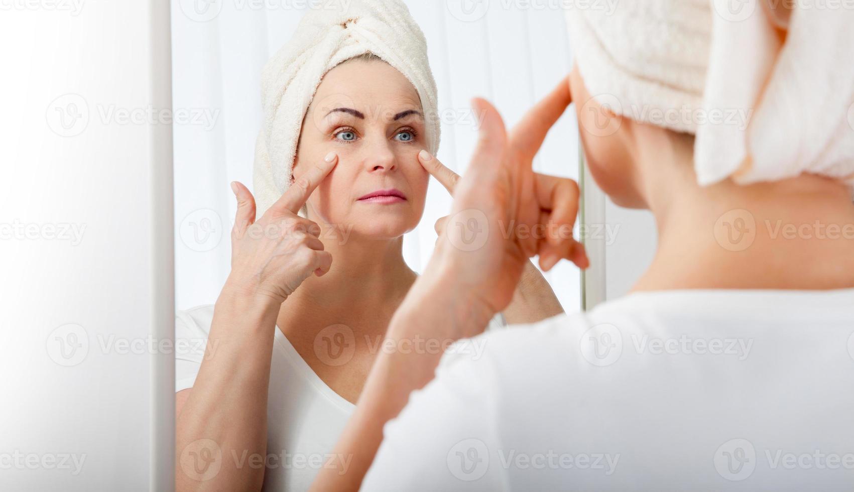 Middle aged woman looking at wrinkles in mirror. Plastic surgery and collagen injections. Makeup. Macro face. Selective focus on the face. photo