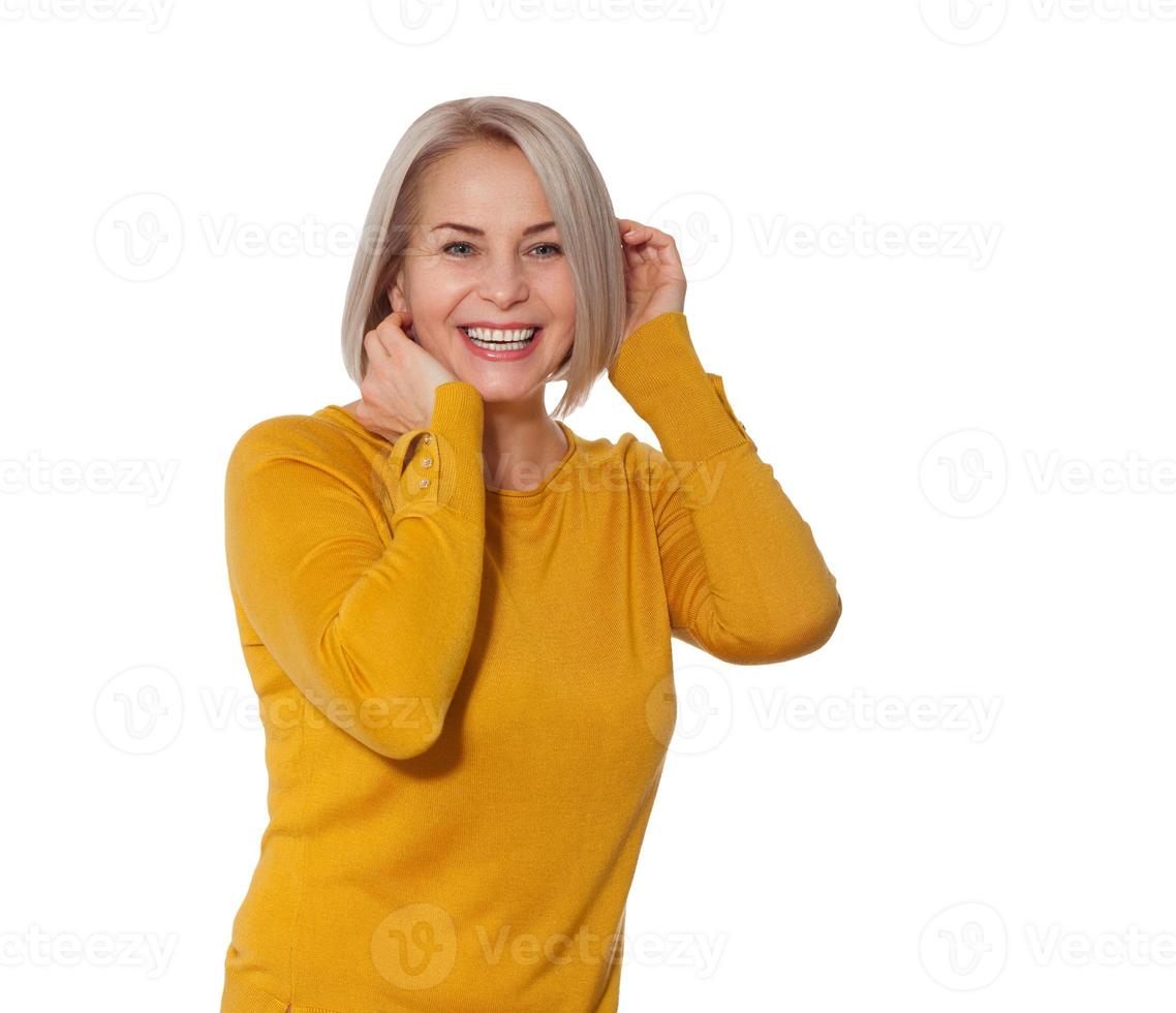 Middle aged blonde emotionally posing in a studio. Happy woman in yellow bright sweater on white background photo