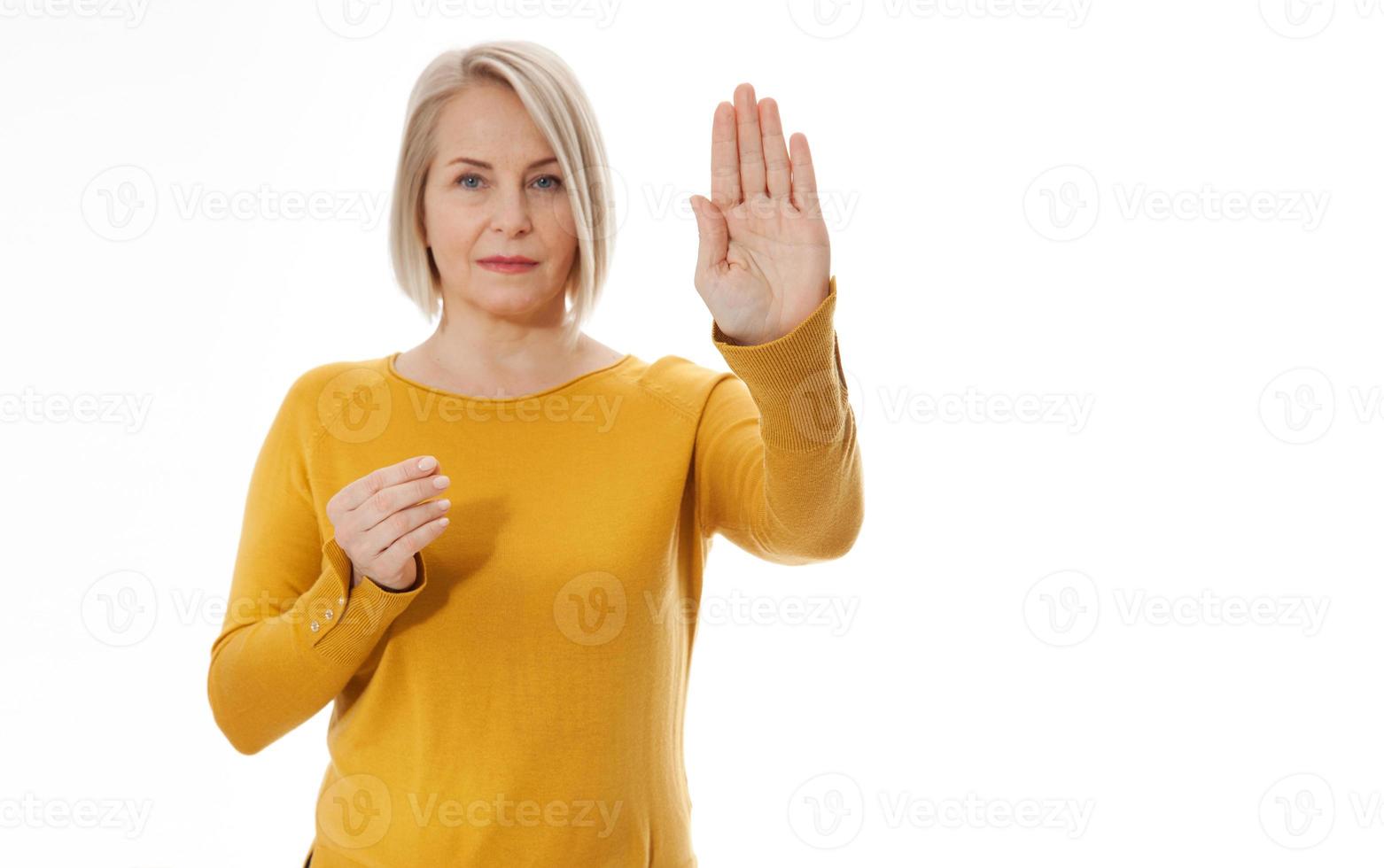 Attractive middle aged woman in a bright yellow sweater holds an empty hand for an anti-advertisement product. Excited woman showing the sign of stop photo