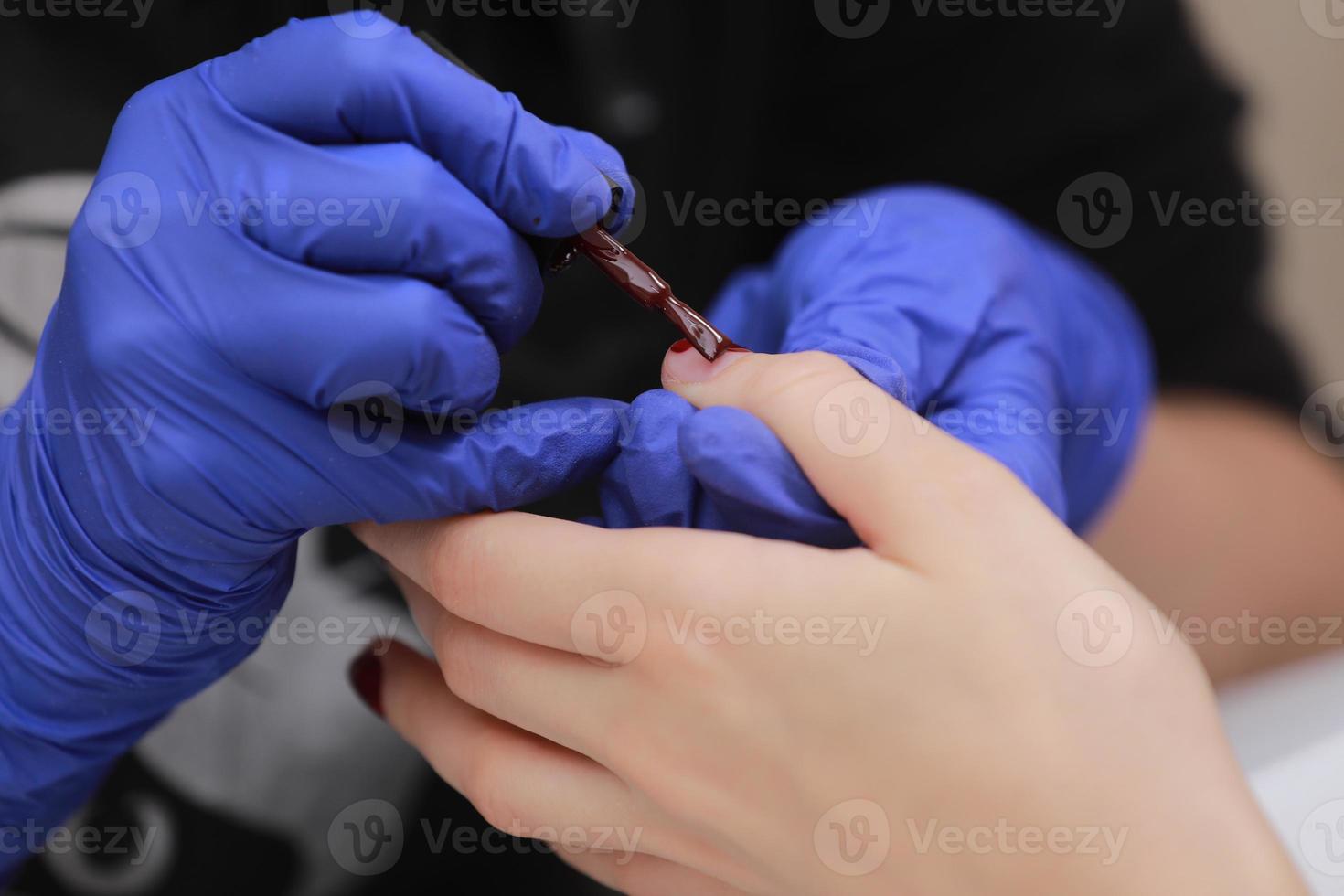 maestro en guantes protectores durante una manicura en el salón de belleza. el maestro manicurista barniza el gel marsala en las uñas de una clienta. el concepto de belleza y salud. foto