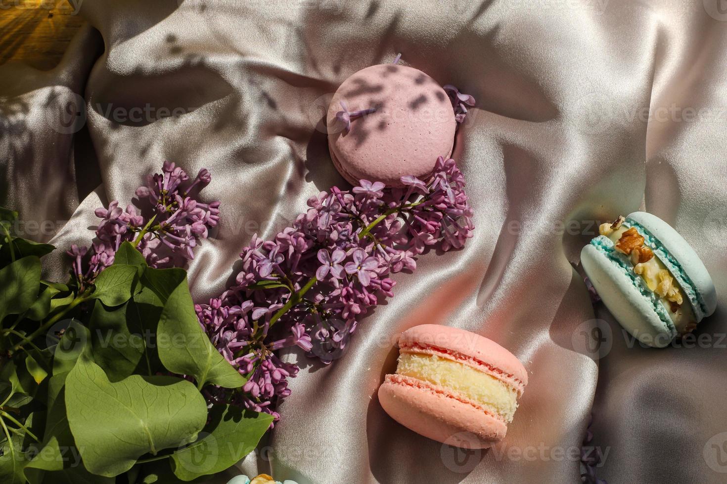 galletas de macarons o macarons franceses de rosa y menta y flores lilas sobre un fondo de tela. sabores naturales de frutas y bayas, relleno cremoso para el día de la madre de san valentín pascua con comida de amor foto