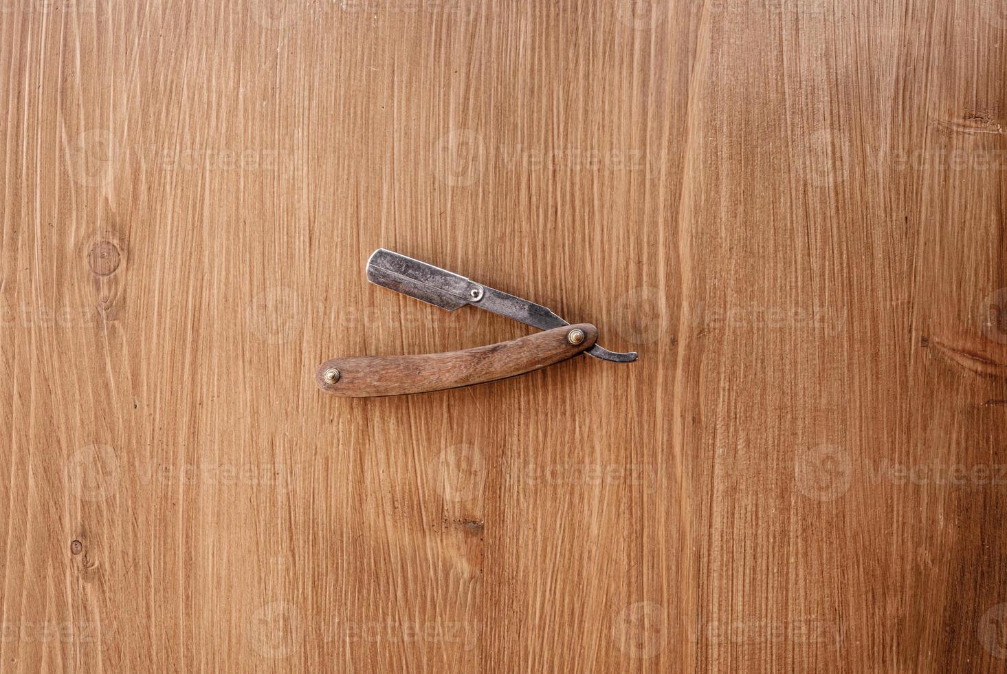 Vintage straight razor with wooden handle isolated on wooden background. Professional barber shop tool. Place for text photo