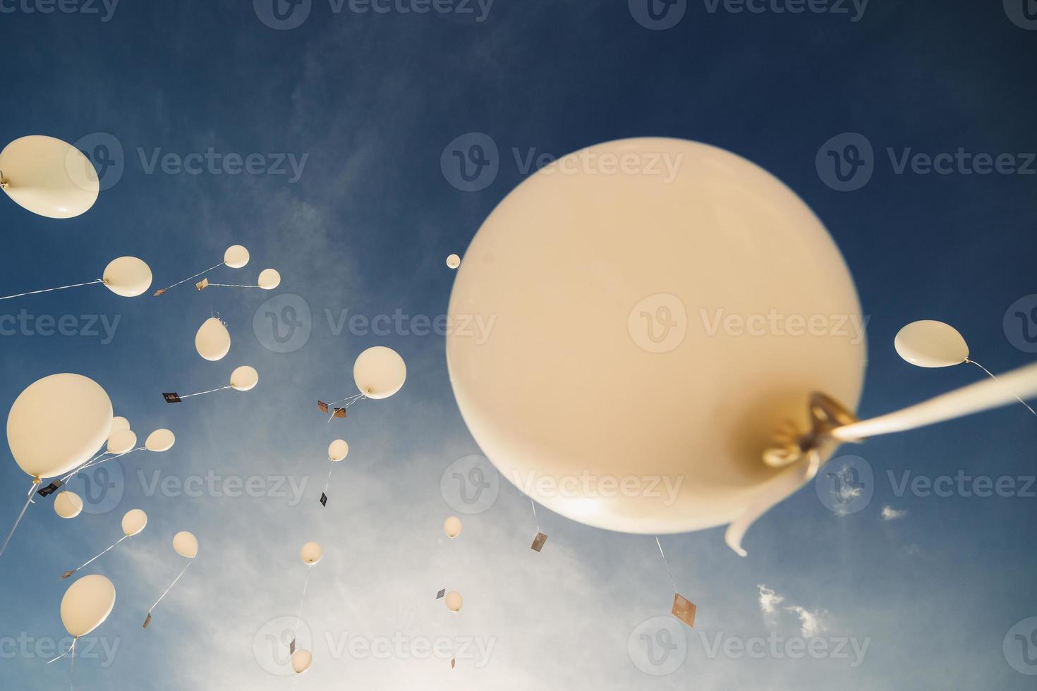 White balloons fly up into the blue sky. The release of festive balloons in the clouds. Celebration and happiness. Air gel balls in the atmosphere. photo