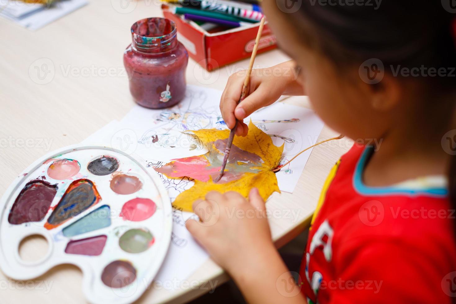 A young beautiful girl is painting autumn maple leaf photo