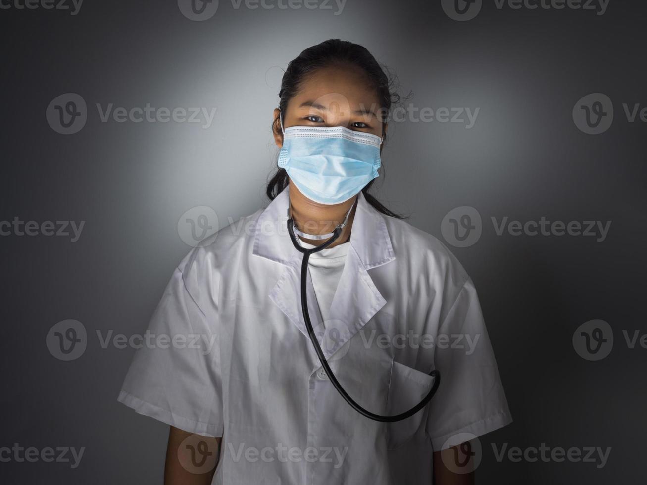 Studio portrait of a female doctor wearing a mask standing on a gray background There was a slight light on his face. photo