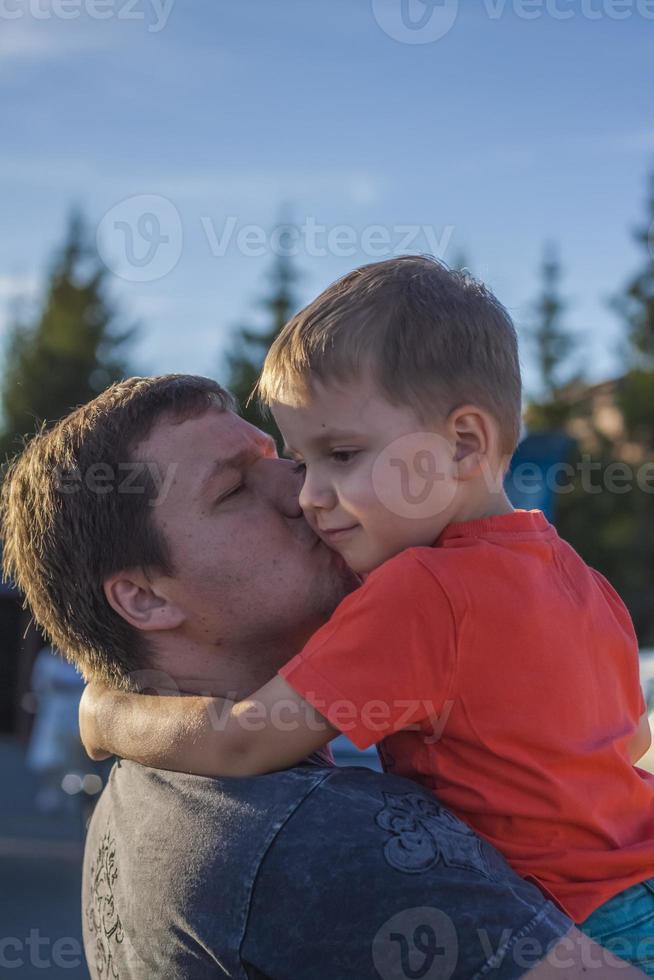 The father hugs and kisses his son on the cheek, whom he holds in his arms. Father and son. photo