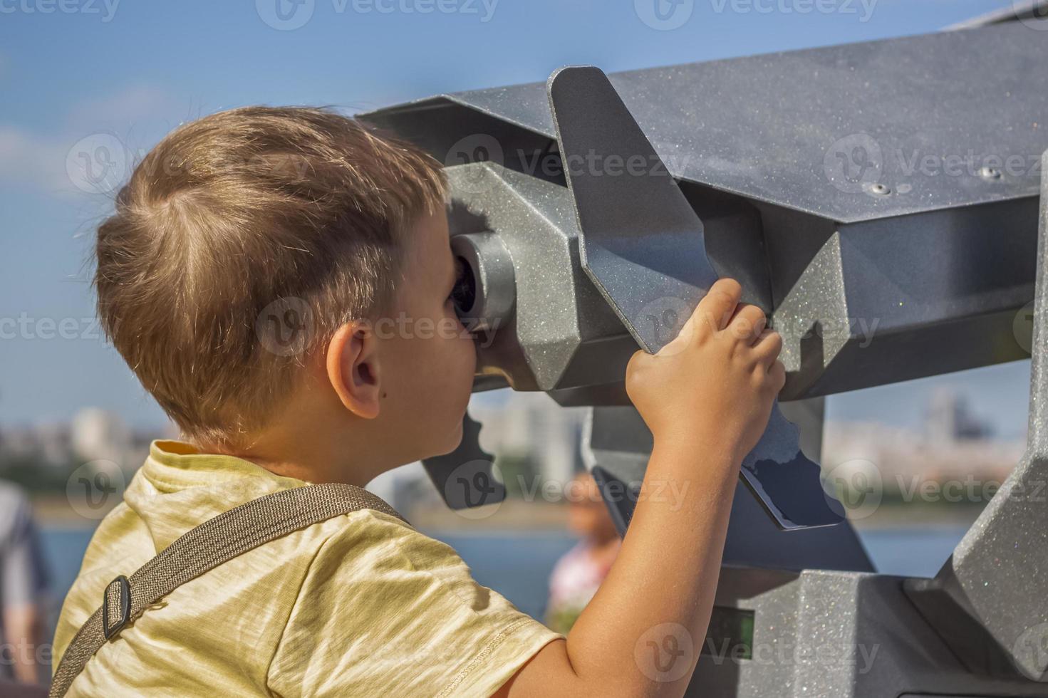 el niño mira a través de binoculares desde la plataforma de observación. viaje. foto