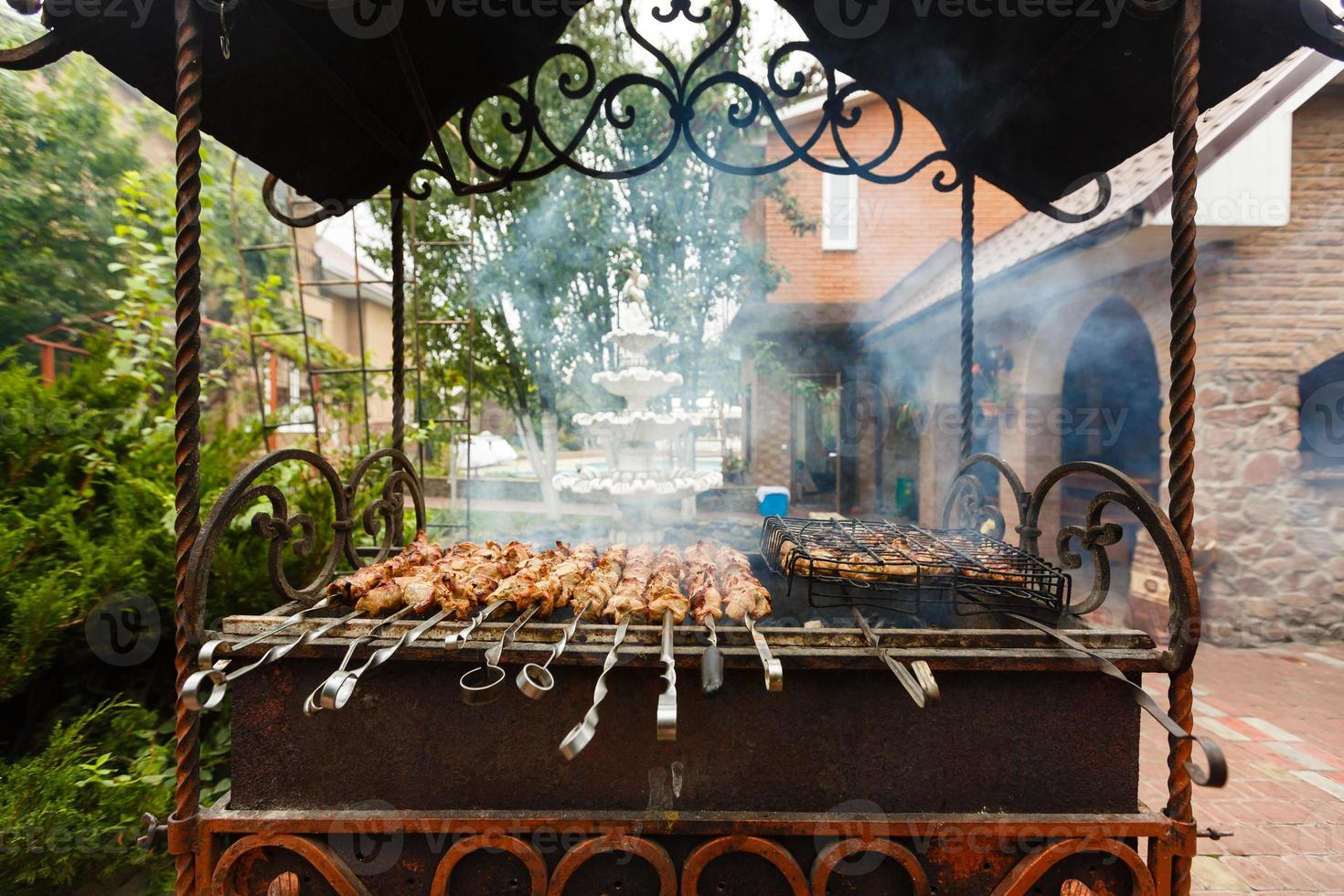 Grilling meat skewers and chicken on natural charcoal barbecue grill. Preparing a big steak on natural firewood BBQ in outside fireplace. photo