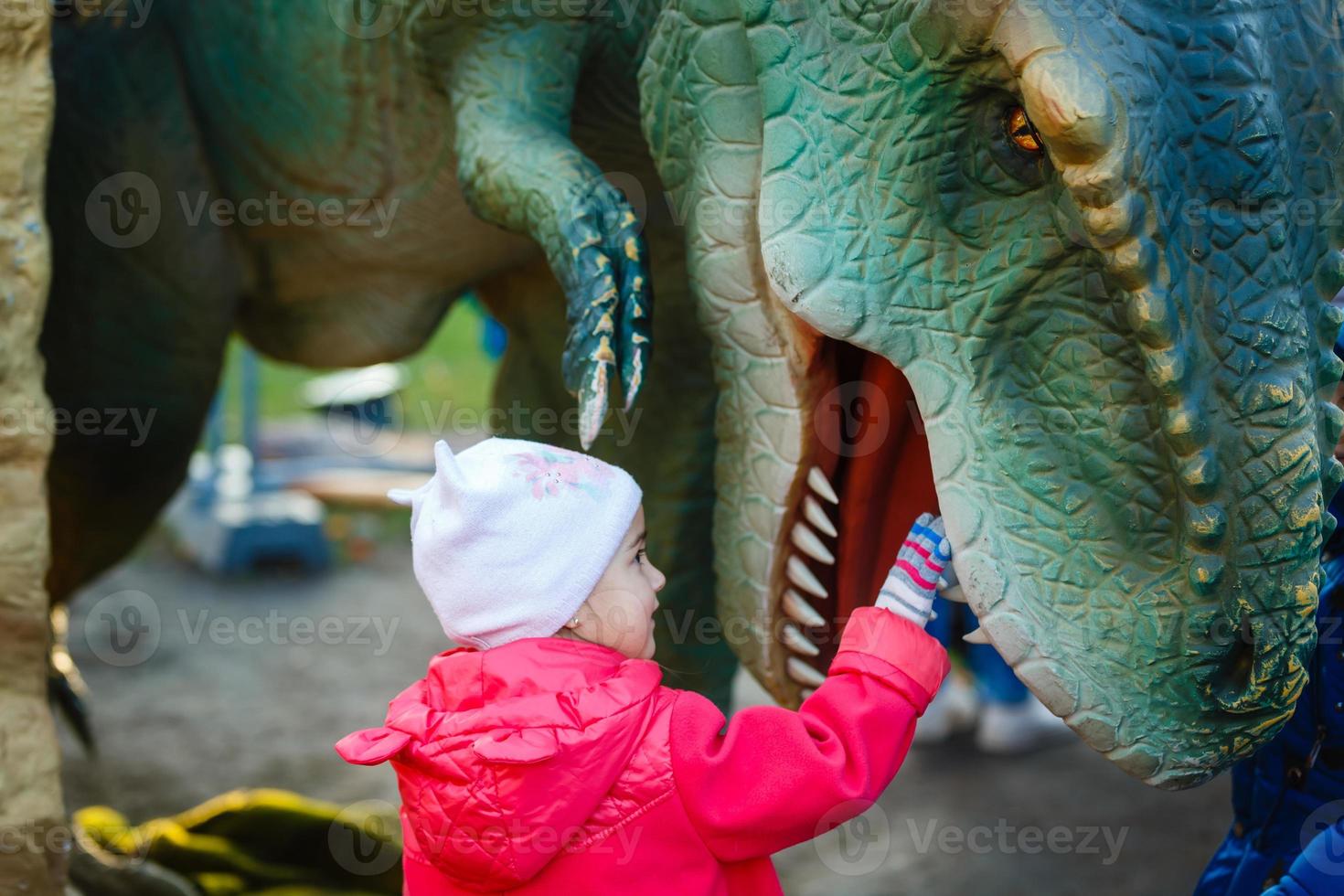 Little girl looking out of the mouth of a dinosaur replica in an amusement park photo