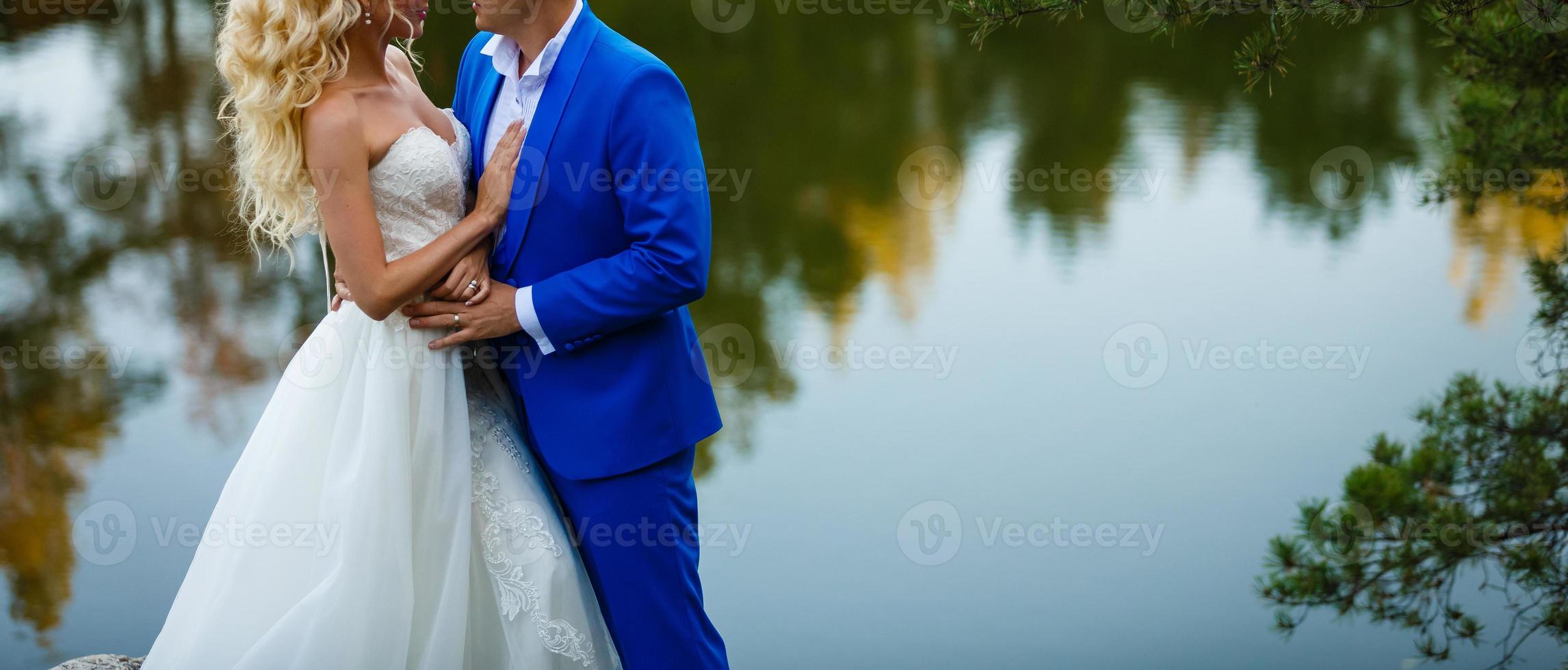 una joven pareja de recién casados en sus vestidos de novia está de pie en la roca foto