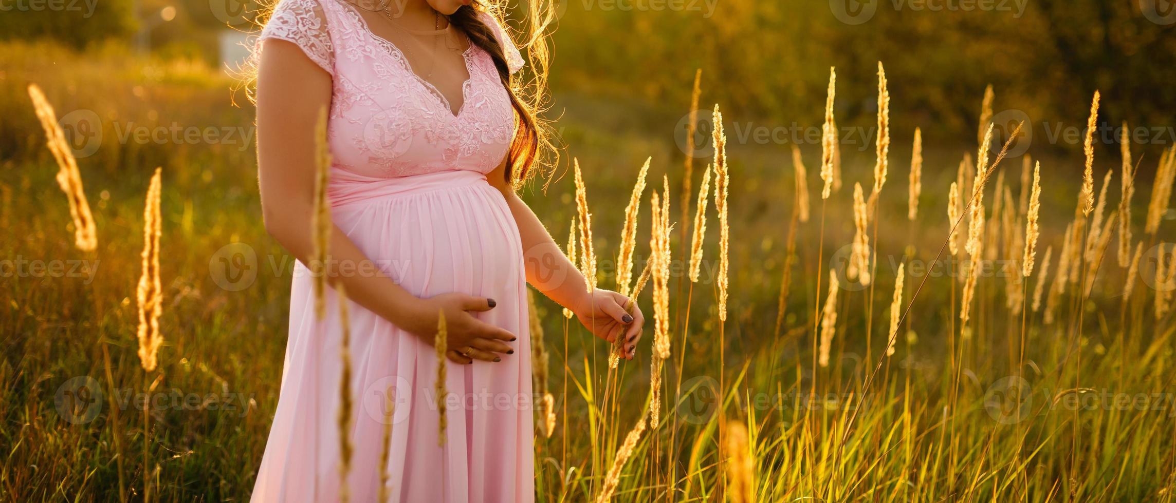 Outdoor portrait of unrecognizable young pregnant woman in the field. beautiful pregnant woman in wreath relaxing in the summer nature meadow. pregnant woman relaxing in flowers photo