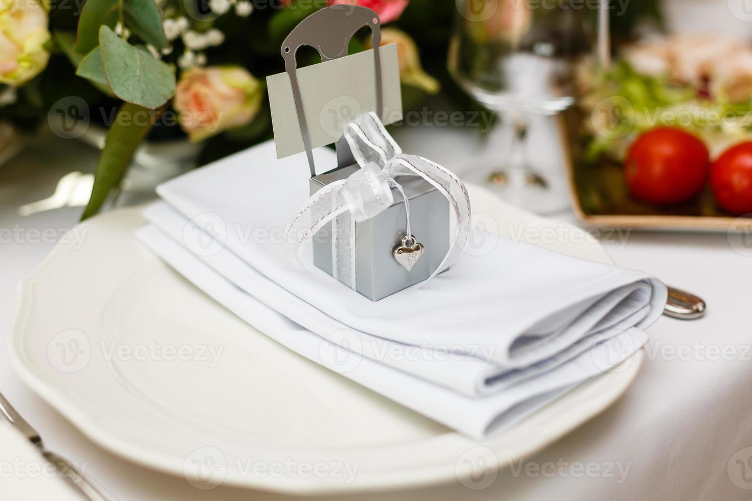 luxury wedding reception. stylish glasses, plates on napkins and silver cutlery and gifts for guest on round table at expensive catering. space for text. decor for feast at holidays photo